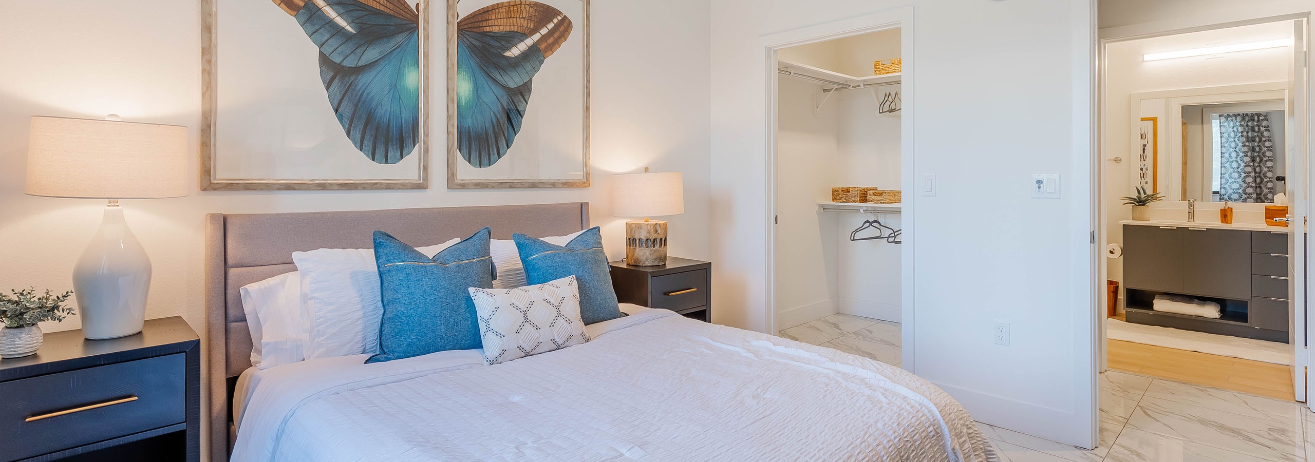 Interior view of AMLI Park West apartment bedroom with a bed centered under butterfly art and two nightstands with lamps