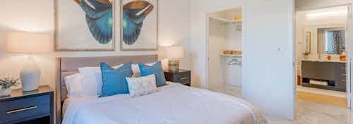 Interior view of AMLI Park West apartment bedroom with a bed centered under butterfly art and two nightstands with lamps