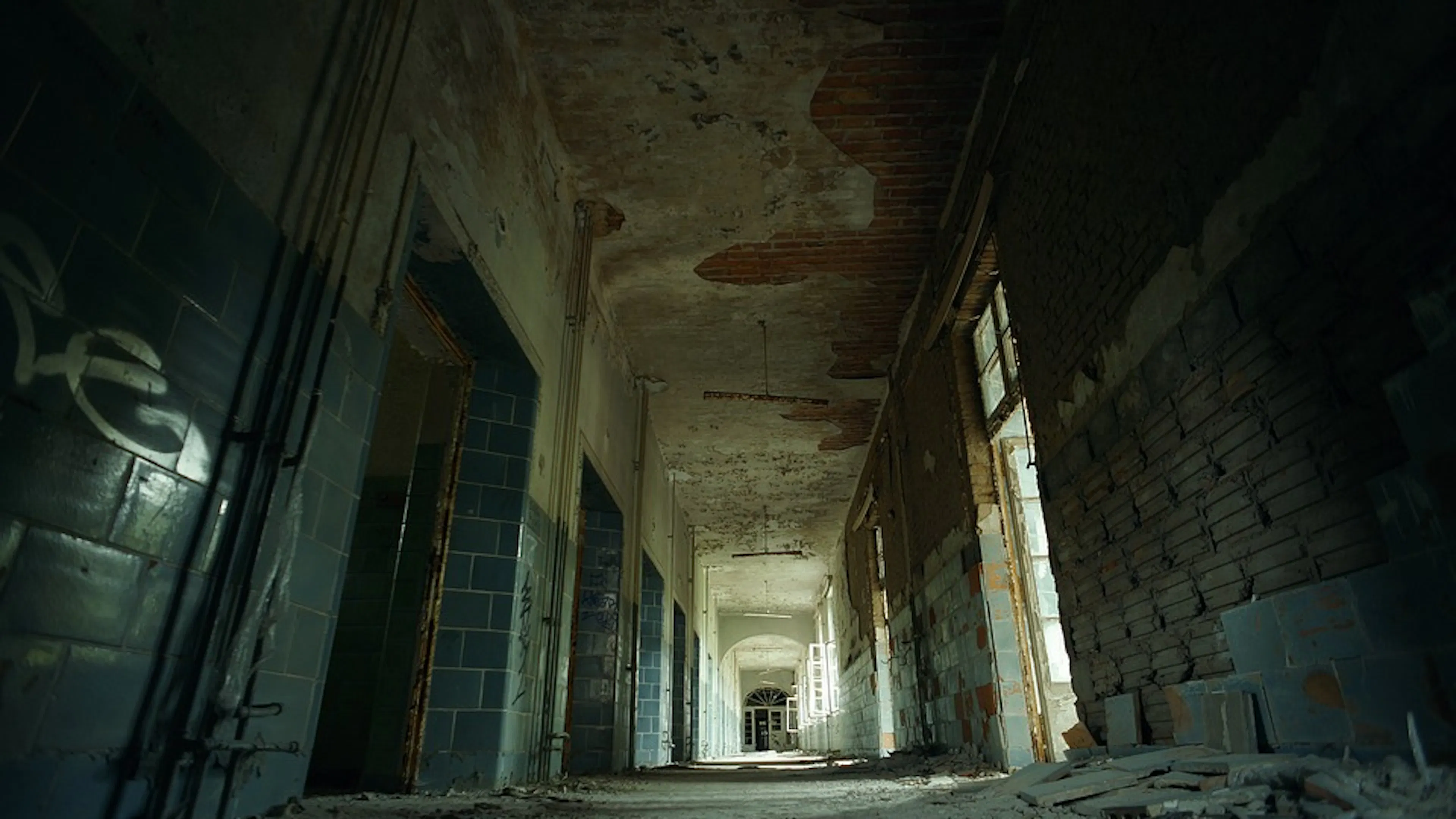 A long hallway in an abandoned hospital with tile and pain peeling off the walls
