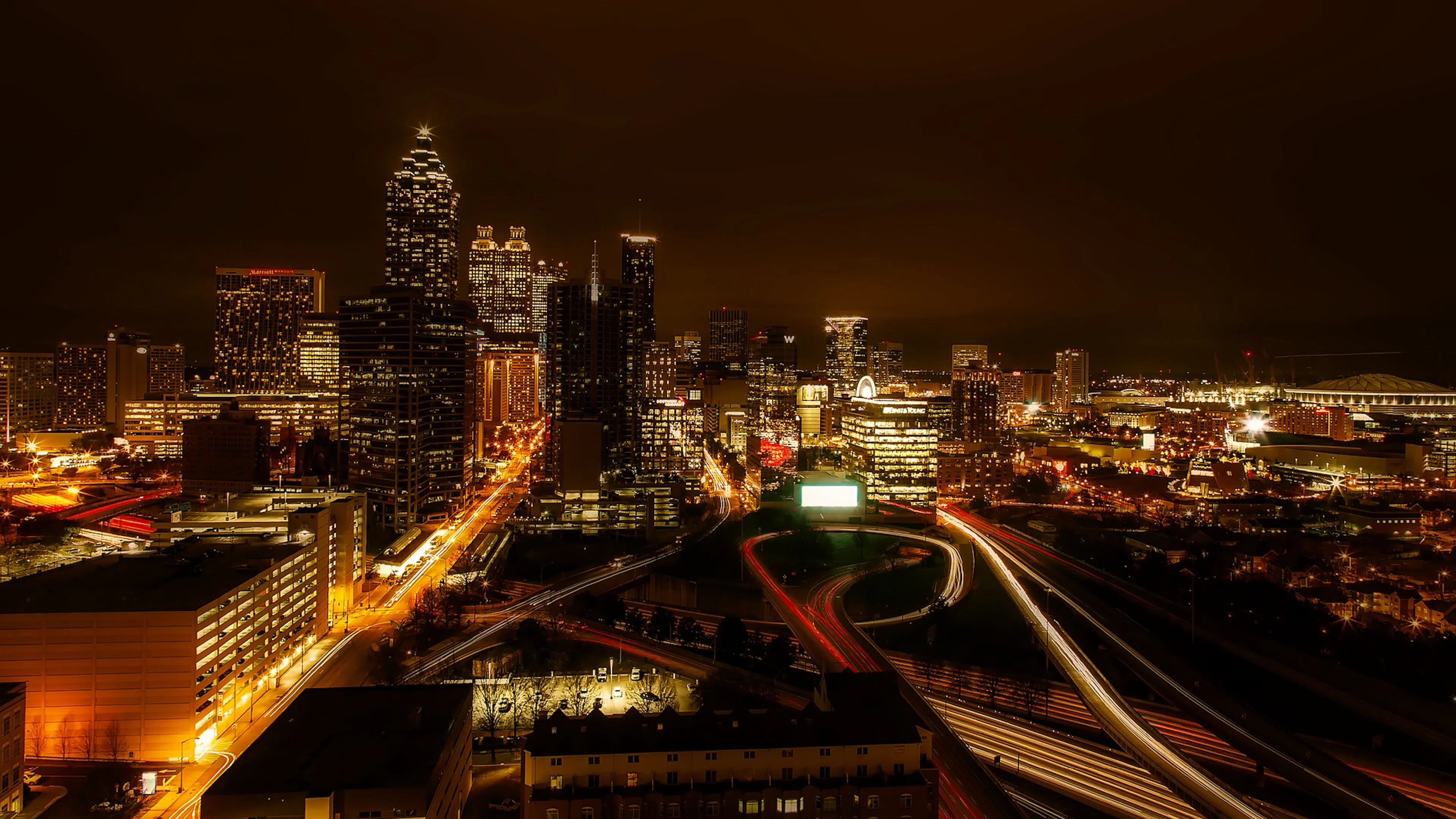 Night time view of the Atlanta skyline with buildings and highways lit up under a cloudy sky