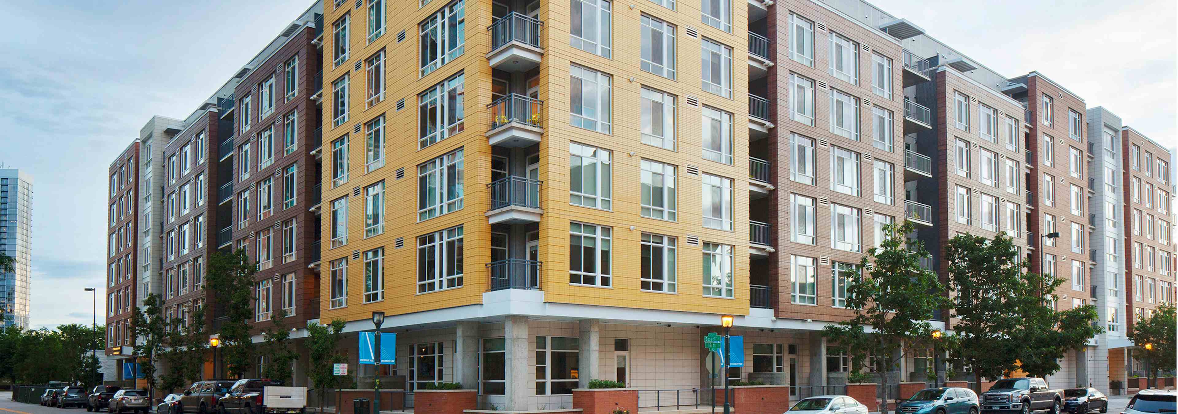 Daytime exterior of AMLI Riverfront Green apartment building with a yellow color scheme as well as parked cars and trees