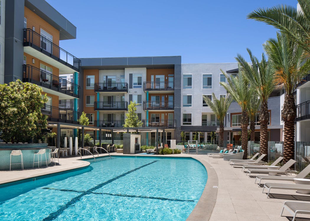 Daytime view of AMLI Uptown Orange swimming pool area with lounge seating and cabanas with individual TVs and palm trees