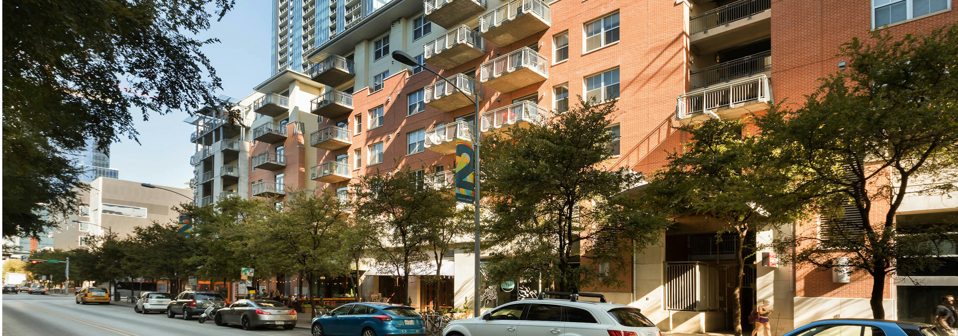 AMLI Downtown apartment community exterior with tree shadows up close and cars parallel parked along the side of the building