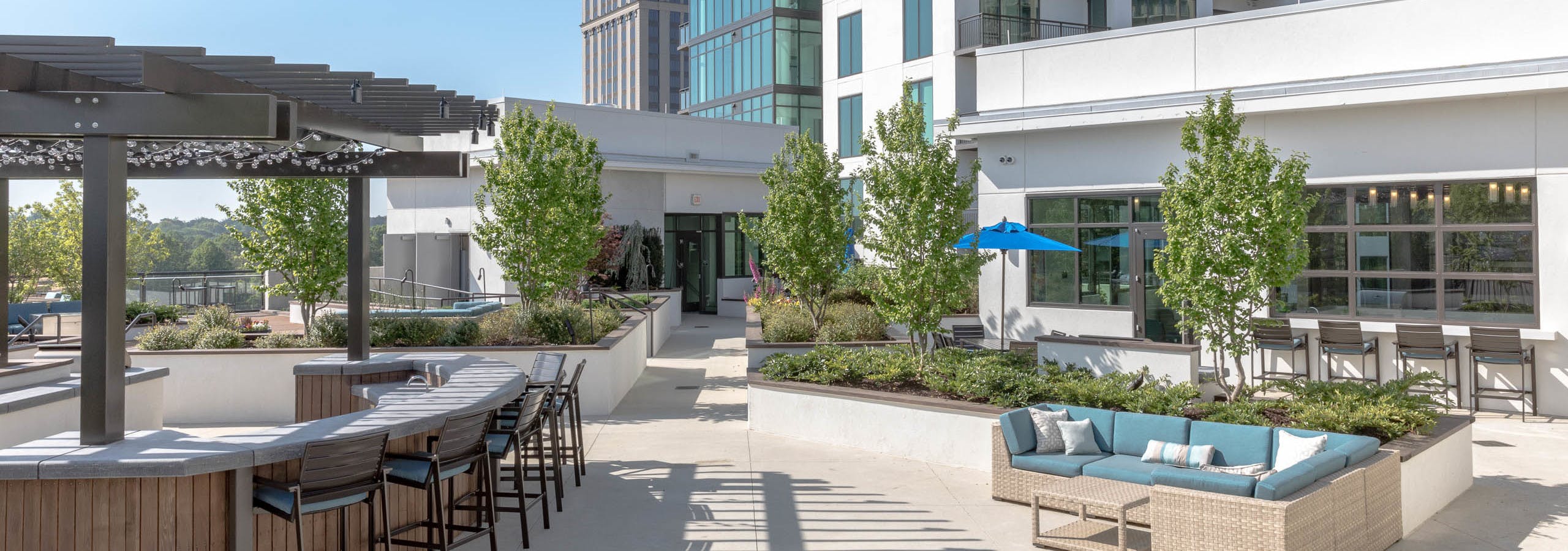 AMLI 3464 rooftop with barstool seating and blue cushion wicker couch with trees and white building facade in the background