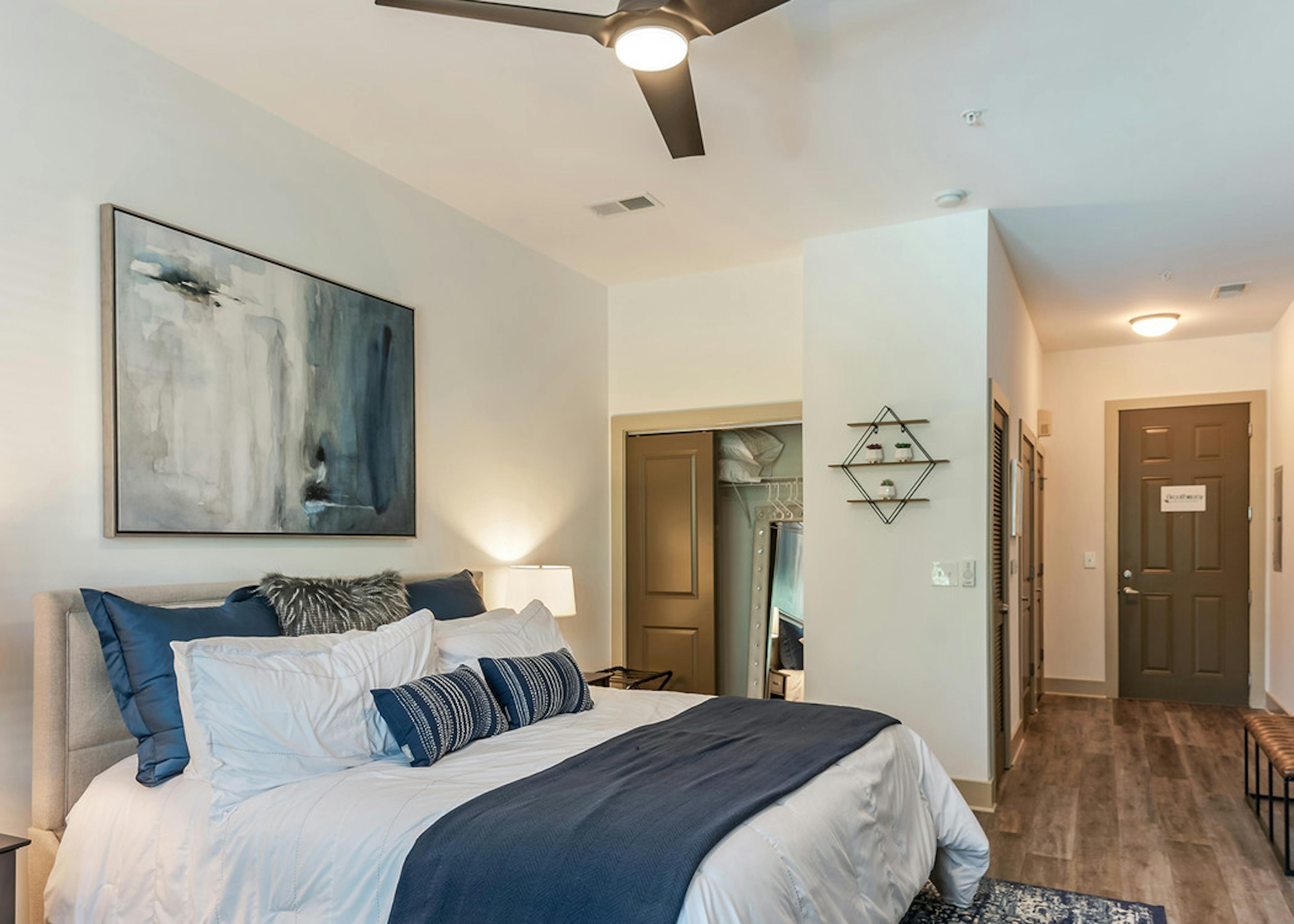 Interior view of AMLI Parkside bedroom with light hardwood and cream walls with blue decor and a peek into walk in closet