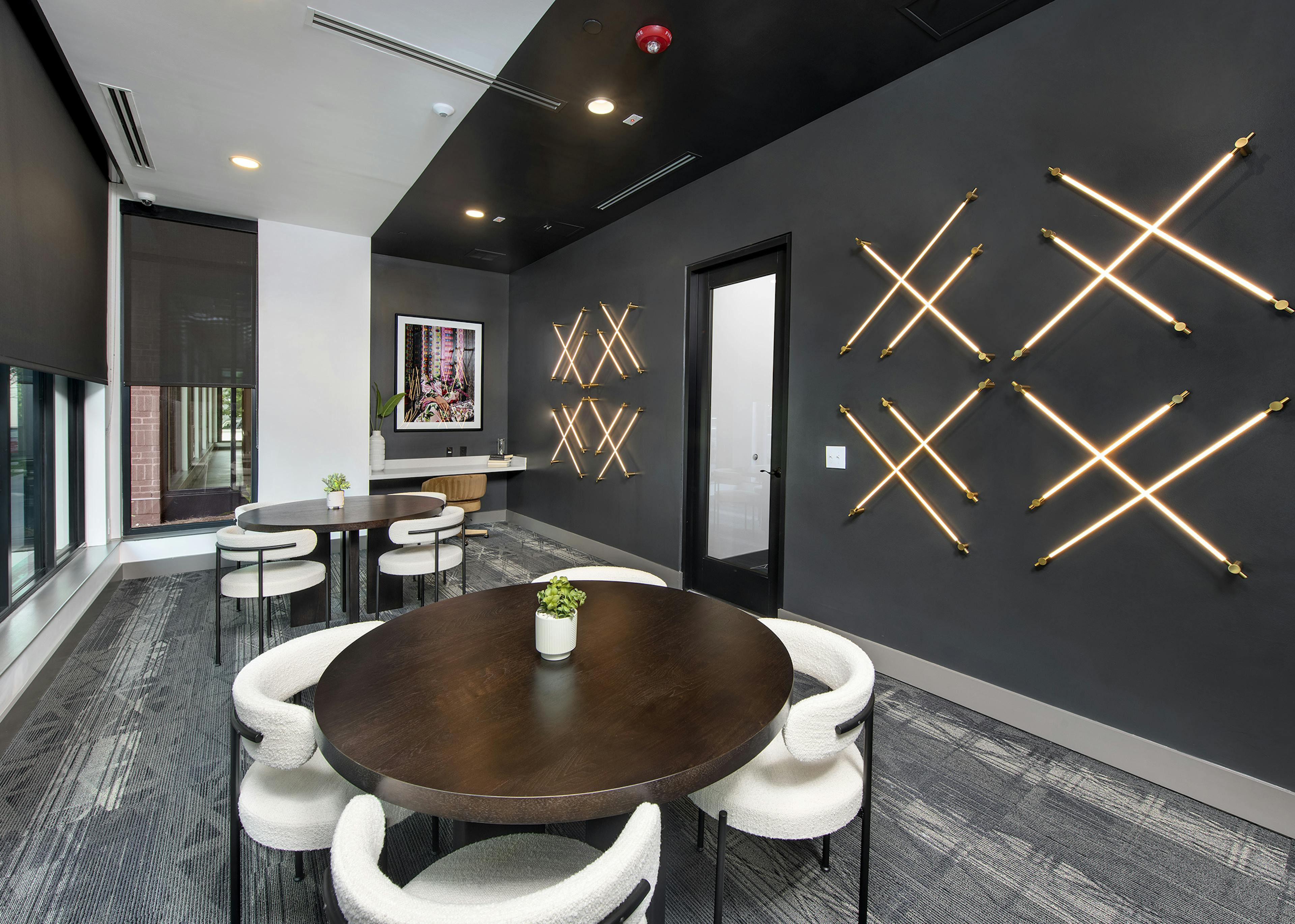 Lounge at AMLI Flatiron with dark grey walls and LED lights in a crisscross pattern with round wood tables and white chairs