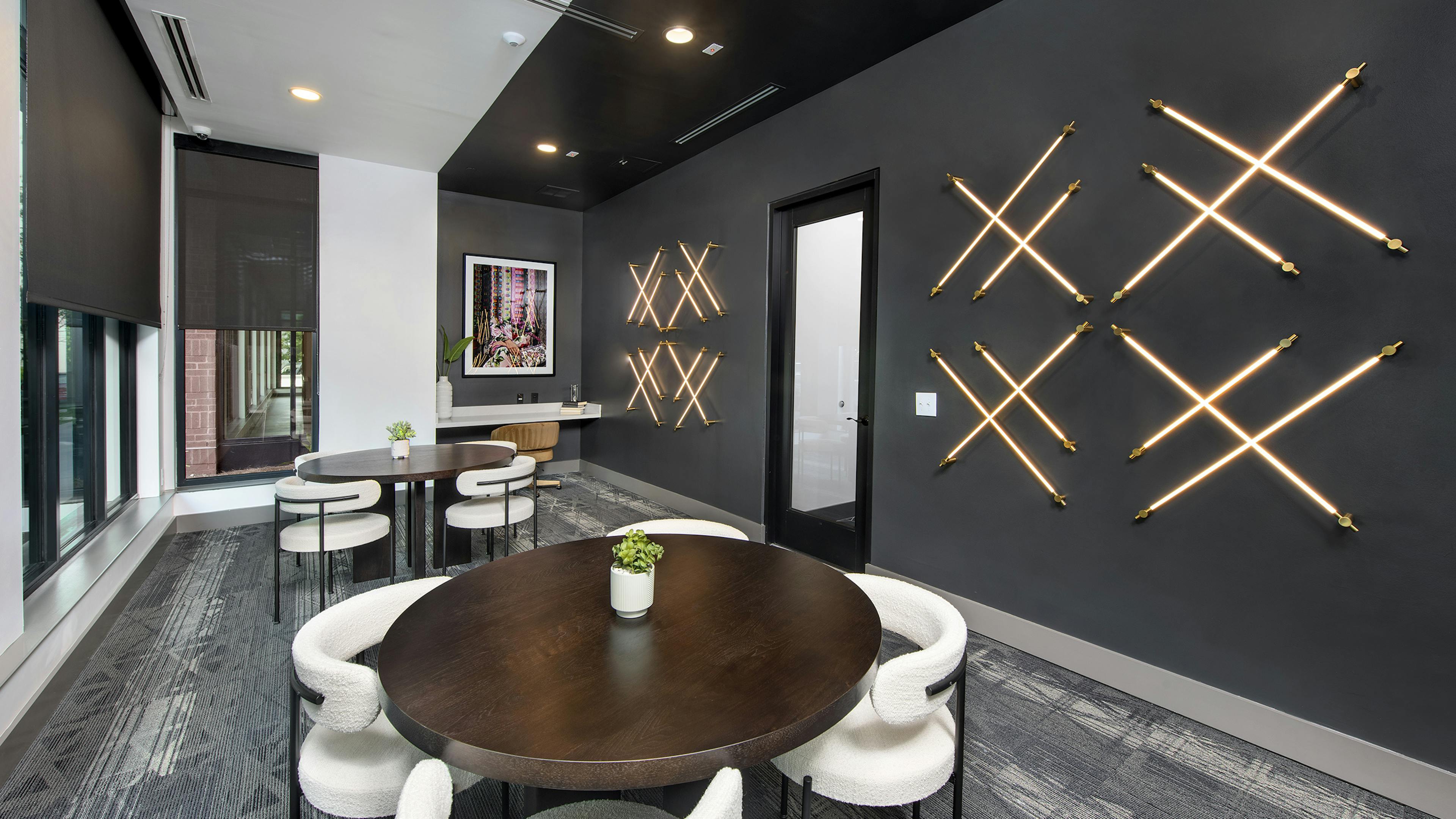 Lounge at AMLI Flatiron with dark grey walls and LED lights in a crisscross pattern with round wood tables and white chairs