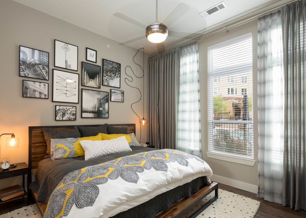 Interior view of AMLI Frisco Crossing apartment bedroom with bed and nightstands and large window with blinds and curtains