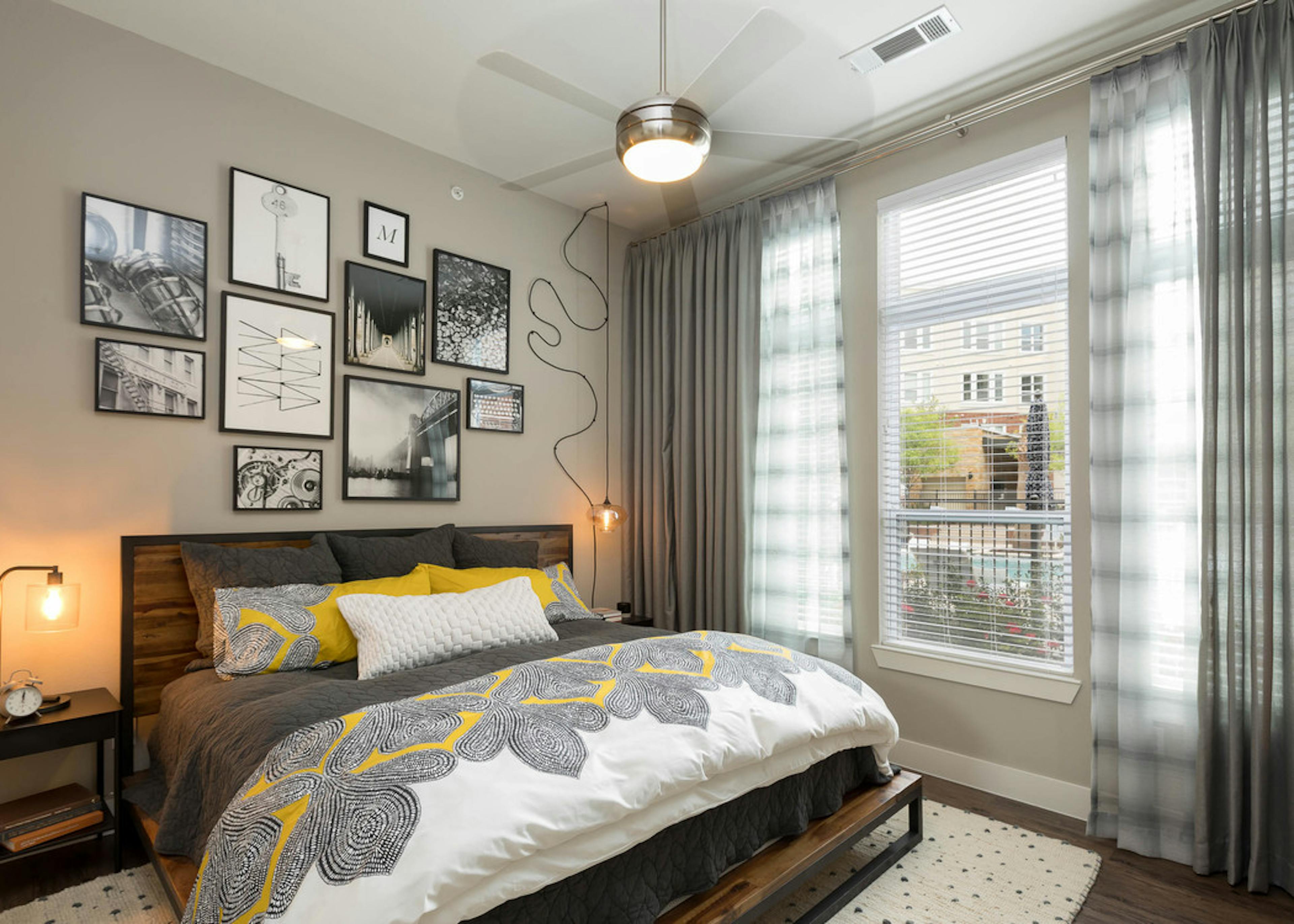 Interior view of AMLI Frisco Crossing apartment bedroom with bed and nightstands and large window with blinds and curtains