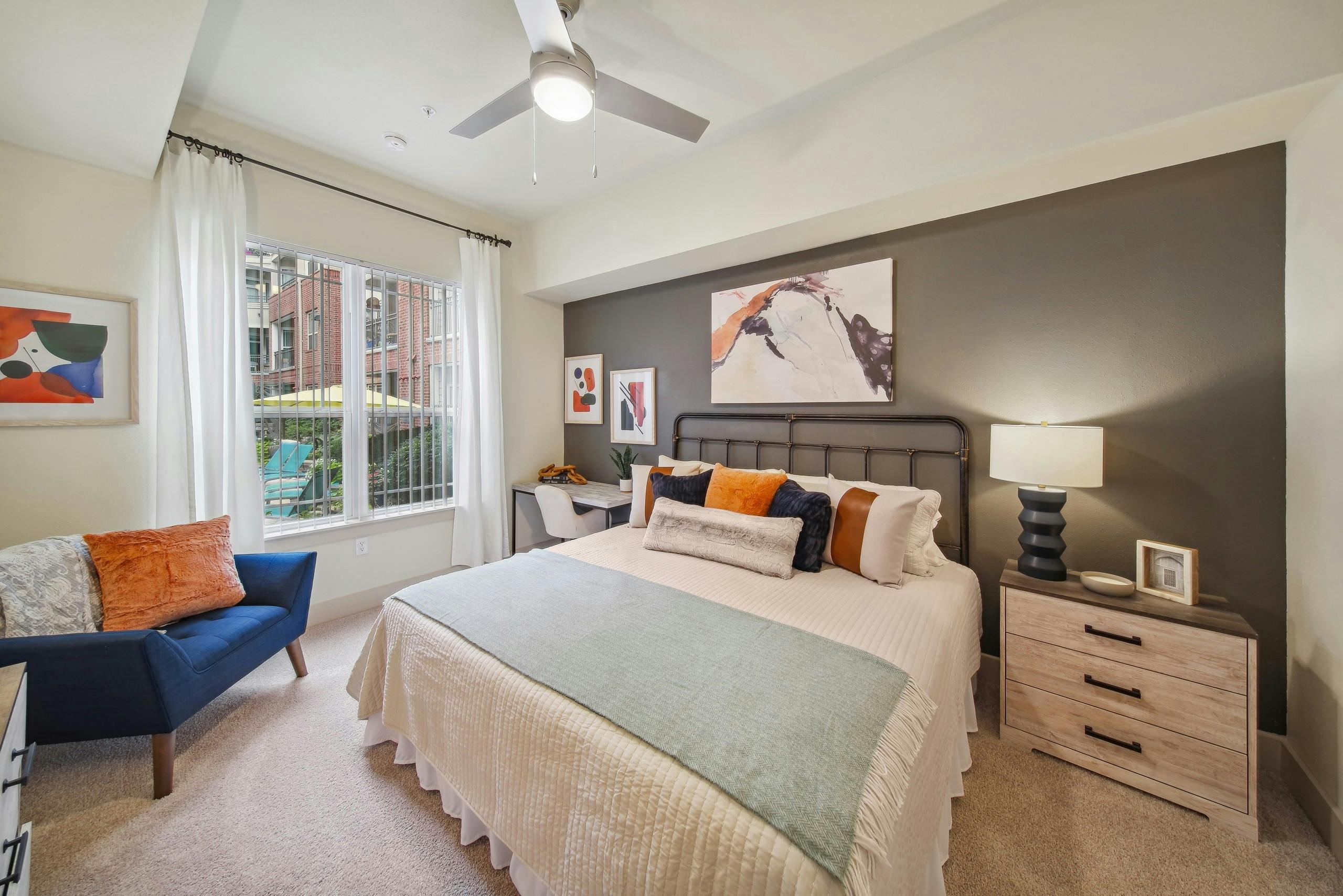 A bedroom at AMLI Park Avenue with a bed and nightstand and desk with a chair and curtained window with view to pool