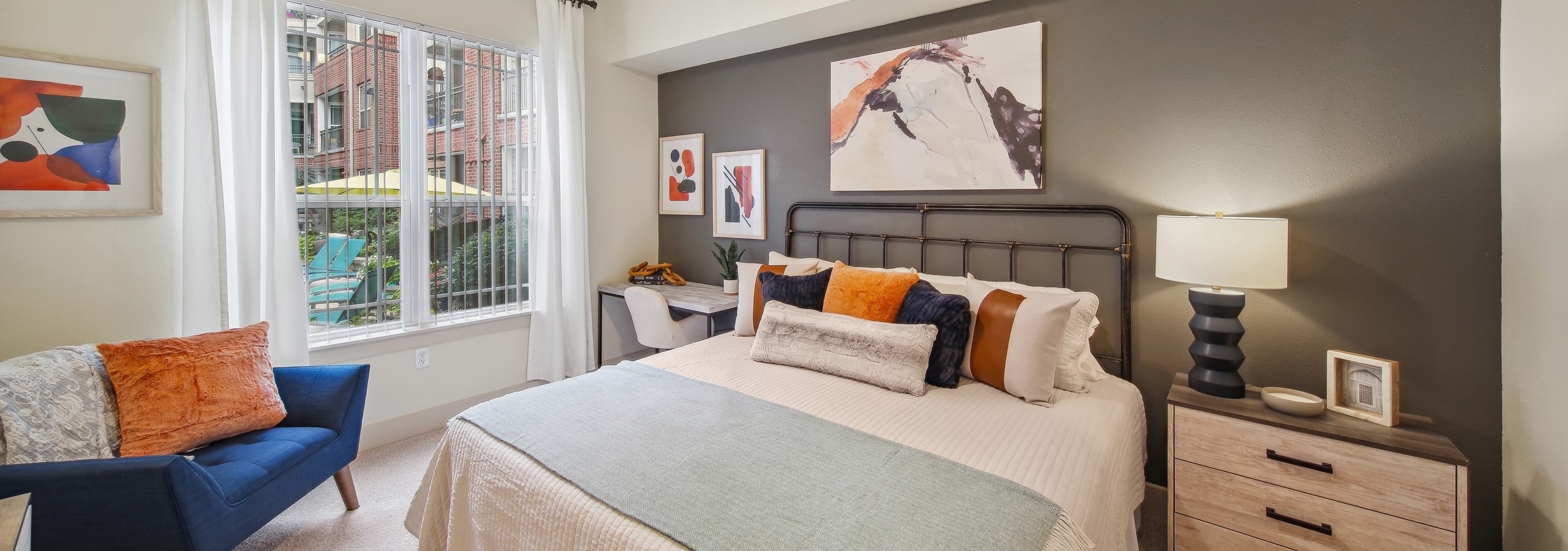 A bedroom at AMLI Park Avenue with a bed and nightstand and desk with a chair and curtained window with view to pool