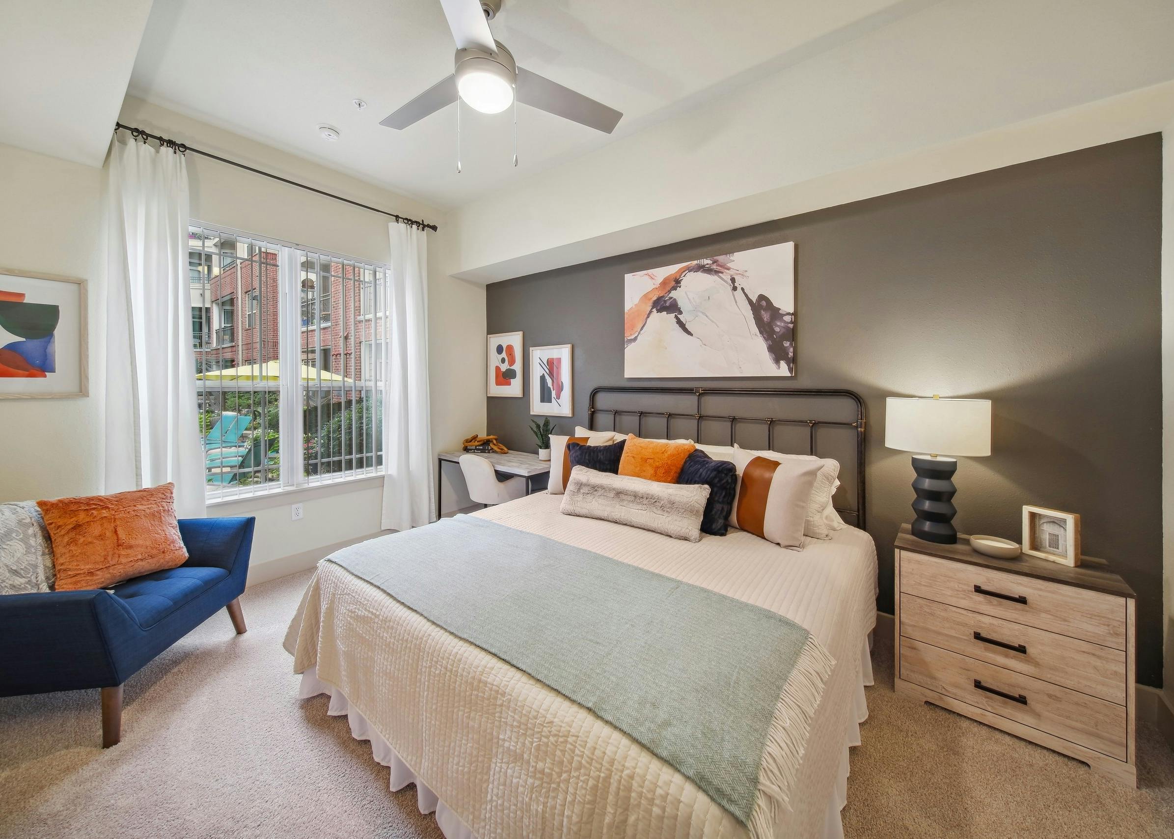 A bedroom at AMLI Park Avenue with a bed and nightstand and desk with a chair and curtained window with view to pool
