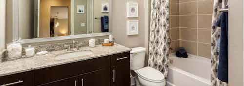 AMLI West Plano bathroom with dark wood vanity sink with a granite countertop and showertub with large beige wall tiles