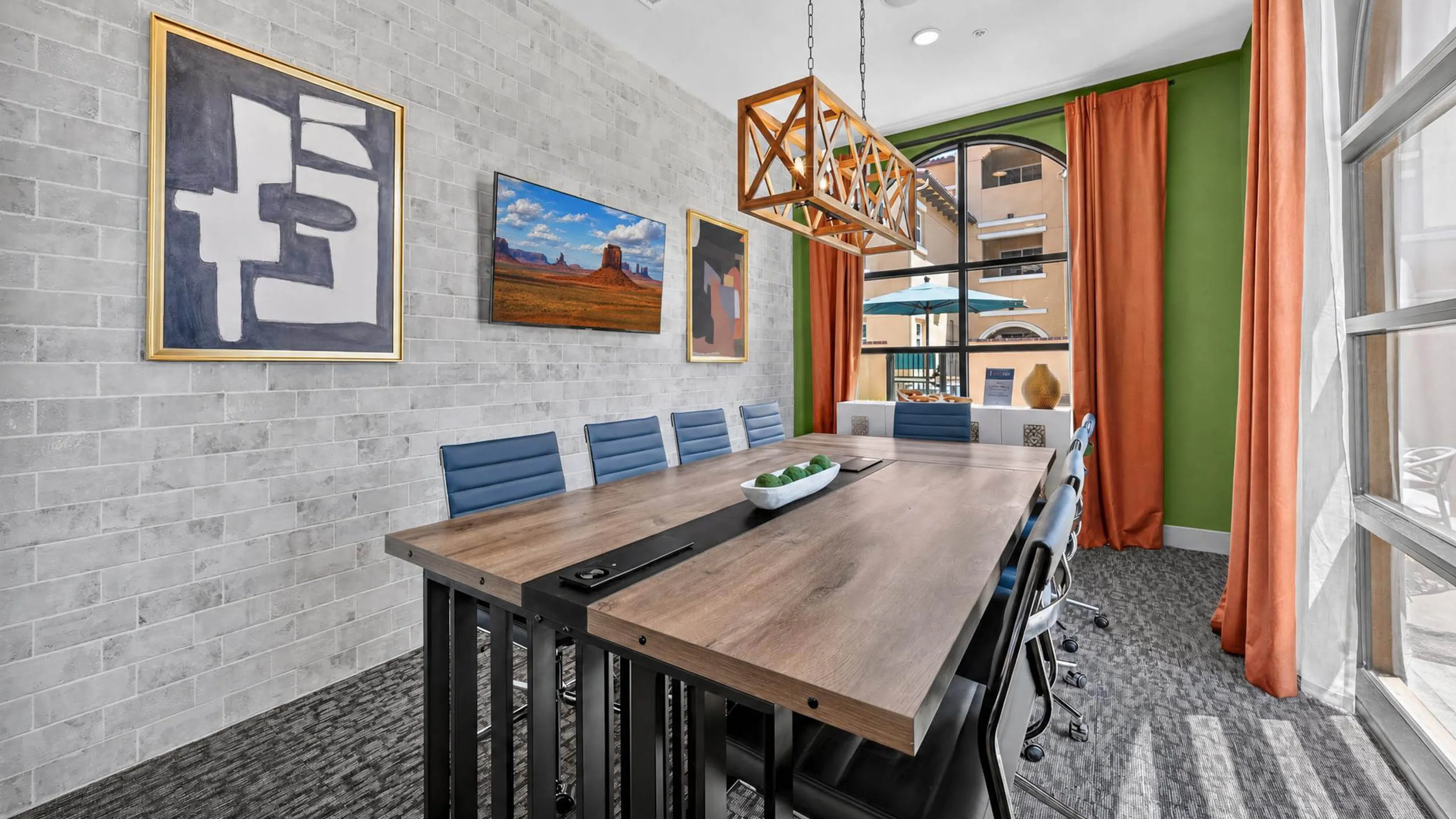 Conference room at AMLI Camarillo apartments with long wood squared table, blue chairs, framed artwork and orange curtains.