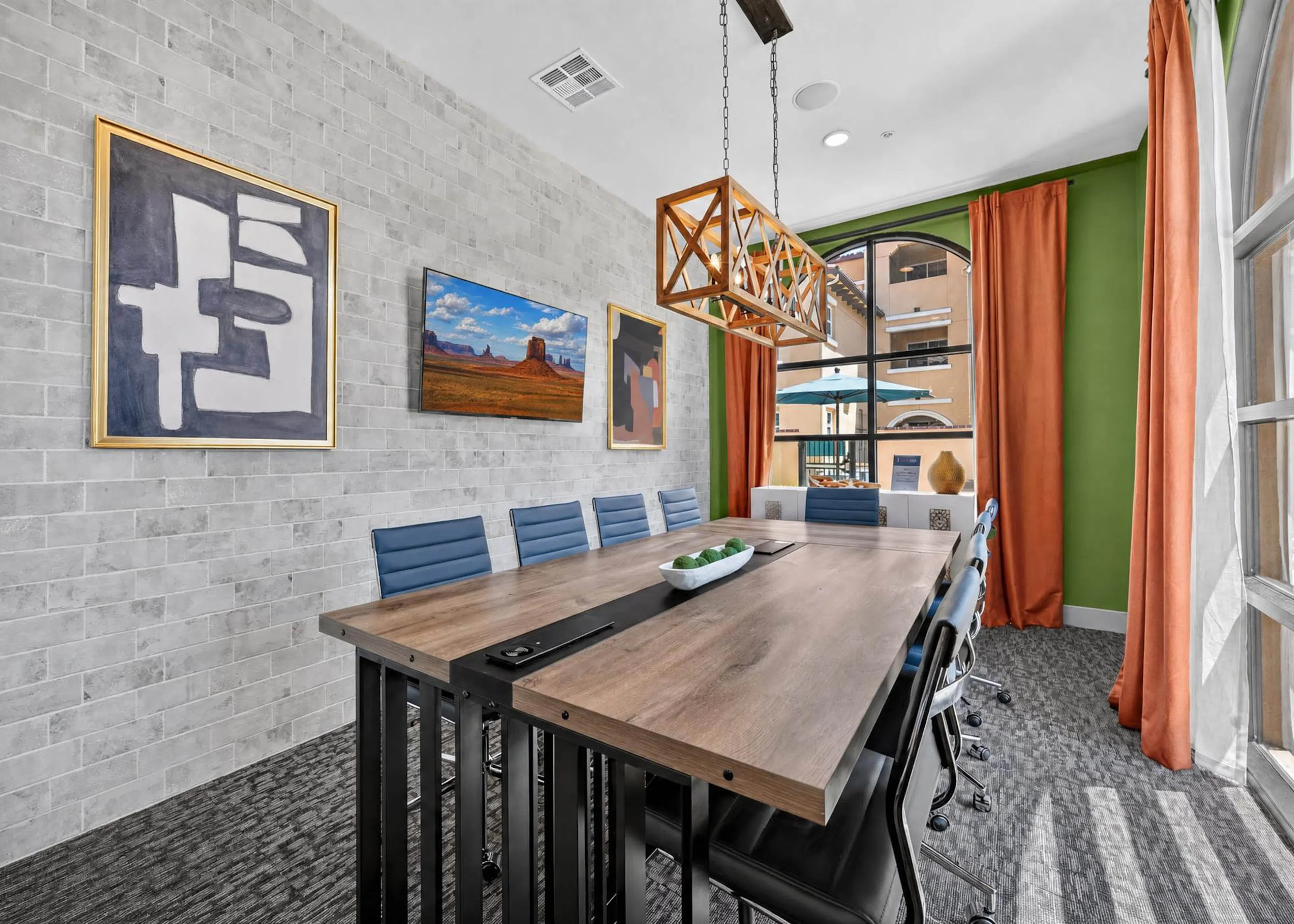 Conference room at AMLI Camarillo apartments with long wood squared table, blue chairs, framed artwork and orange curtains.