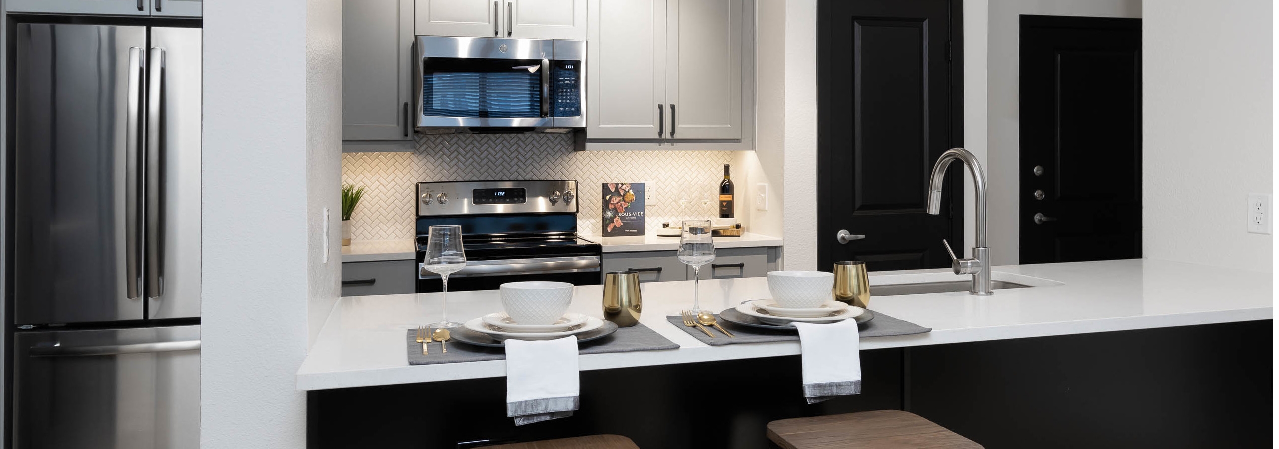 Interior of kitchen at AMLI Quadrangle with grey wood cabinets and a black island with white countertops and beige backsplash