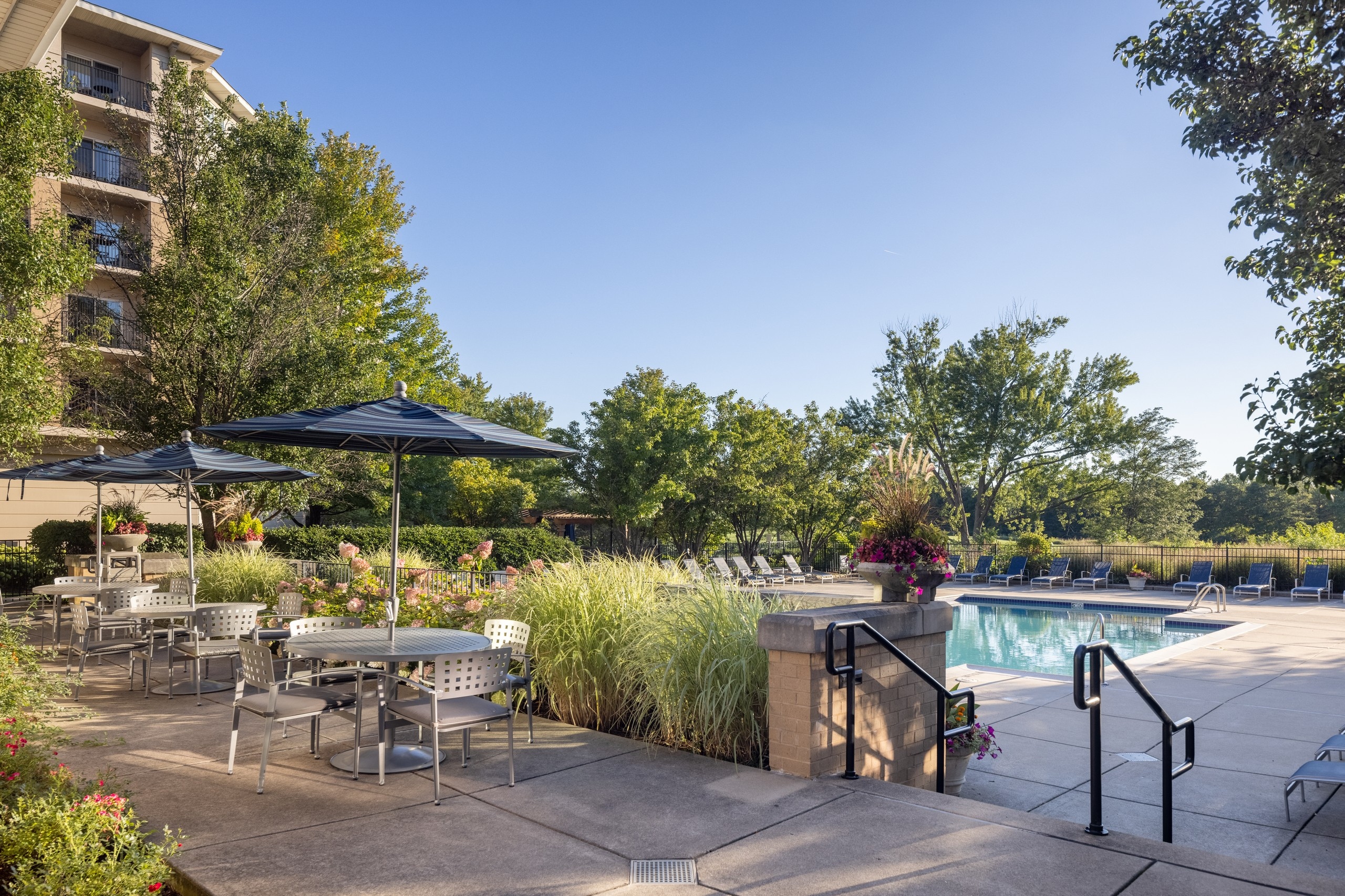 AMLI at Seven Bridges clubhouse terrace with three tables with chairs and blue umbrellas overlooking the pool and golf course