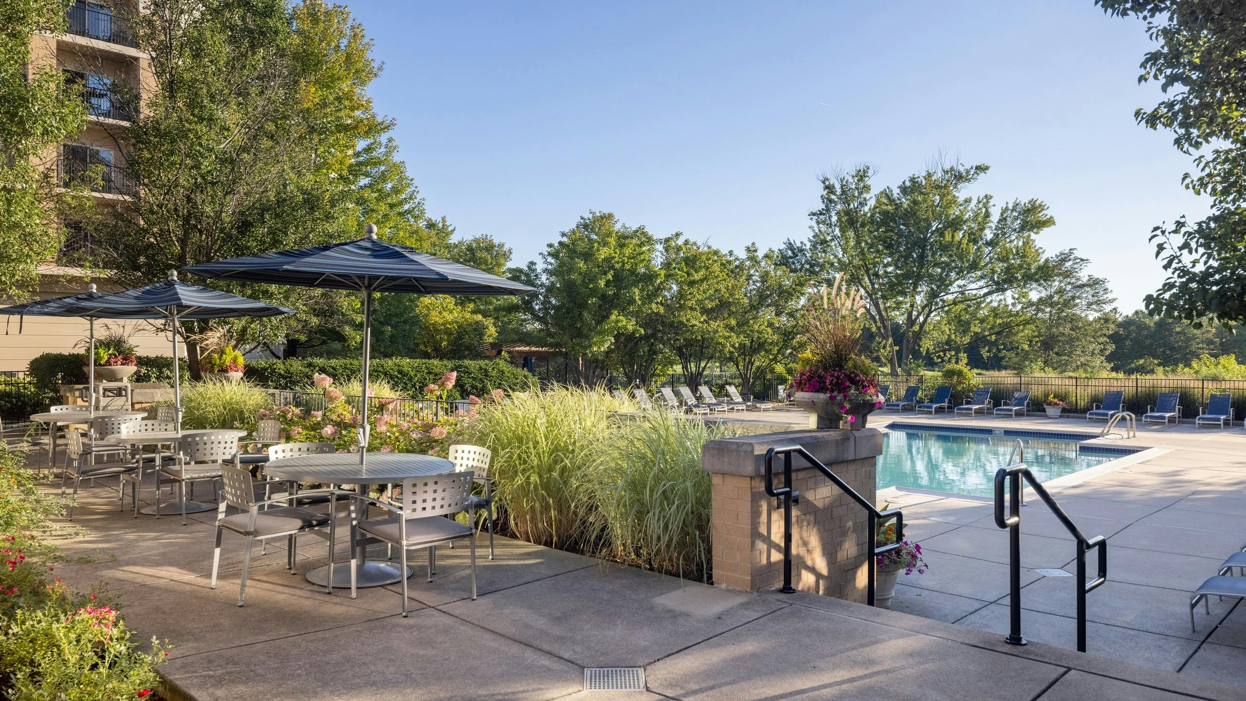 AMLI at Seven Bridges clubhouse terrace with three tables with chairs and blue umbrellas overlooking the pool and golf course