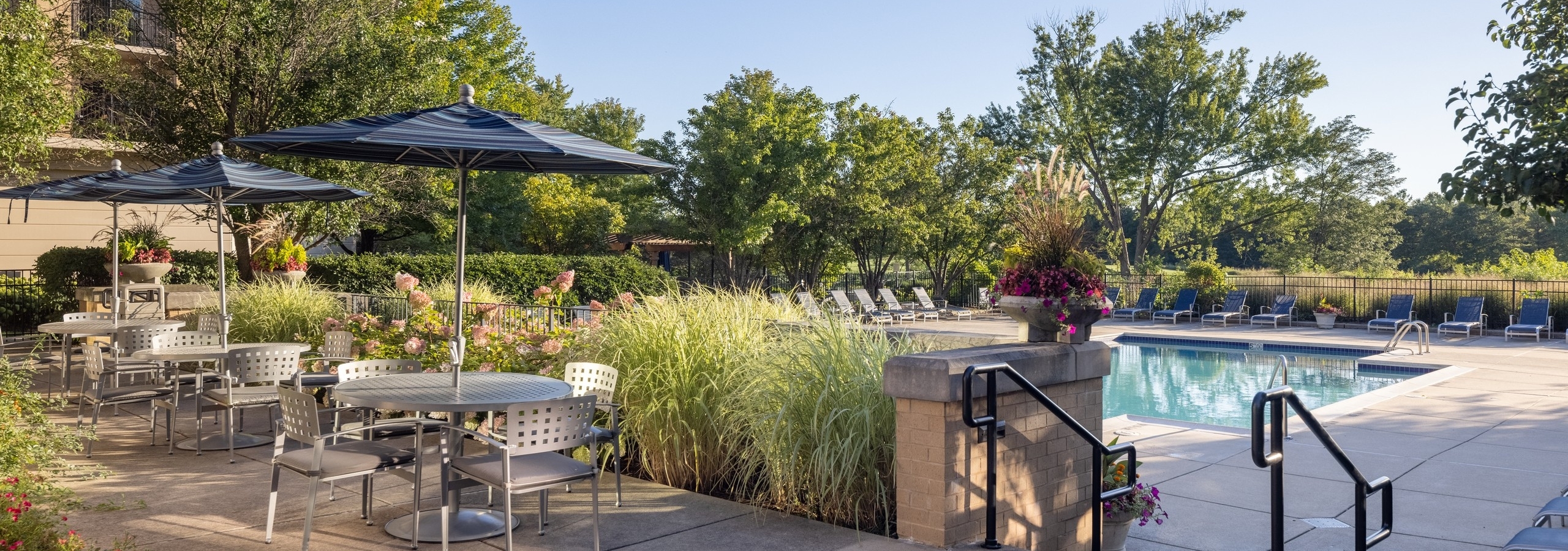 AMLI at Seven Bridges clubhouse terrace with three tables with chairs and blue umbrellas overlooking the pool and golf course