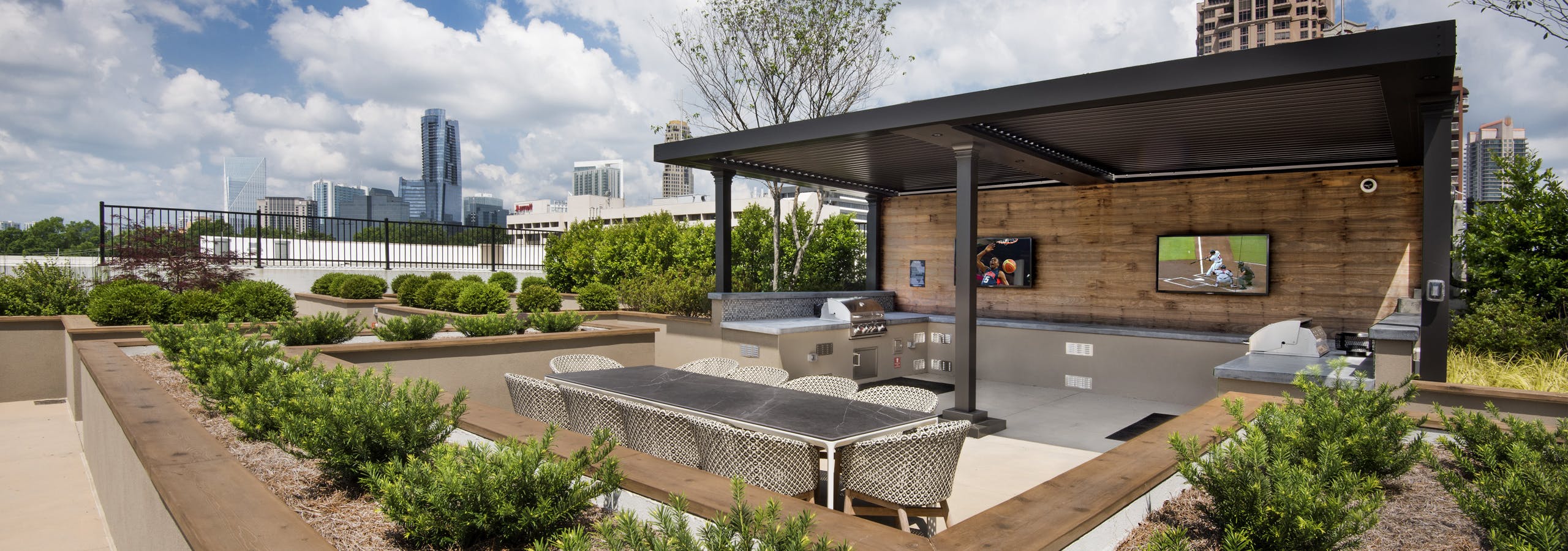 Exterior view of AMLI Lenox rooftop grill area on a bright and sunny day with two grills and two televisions and dining area