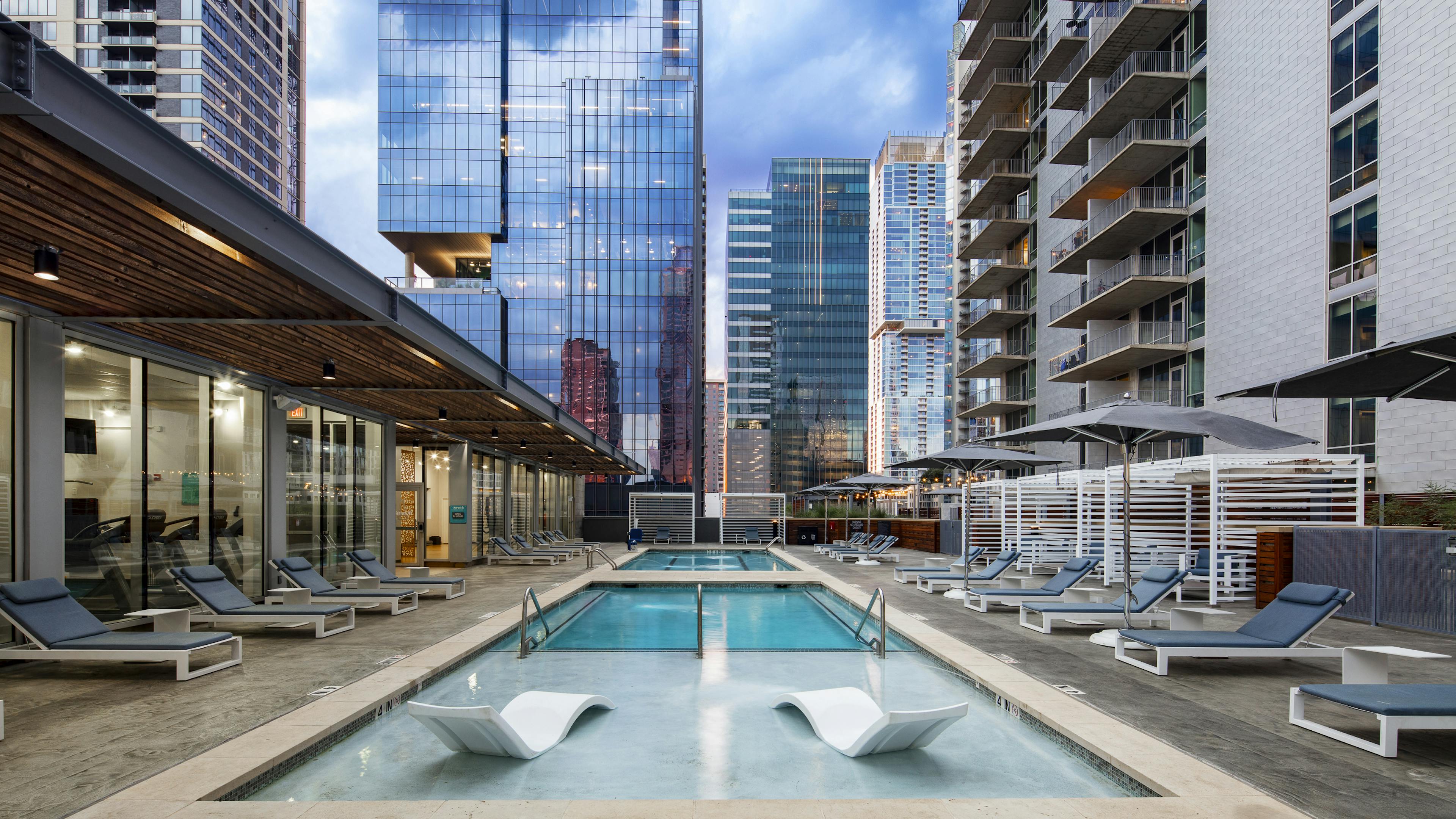 Sunset view of AMLI on 2ND Skye deck pool with lounge seating and two white in-water chairs and white cabanas and city view