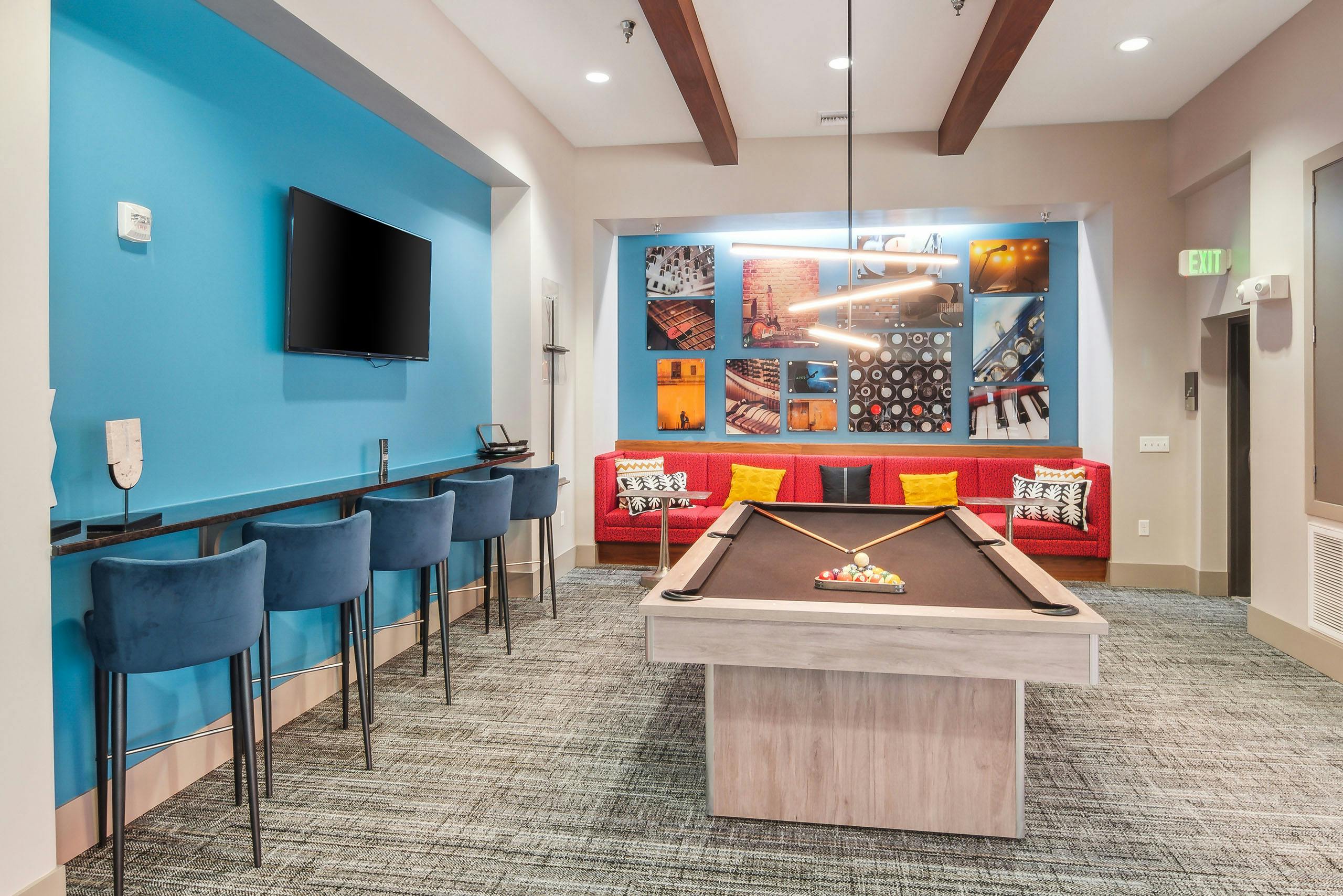 Interior view of the billiards table area at AMLI Denargo Market clubroom with red couch and blue walls with a TV and artwork