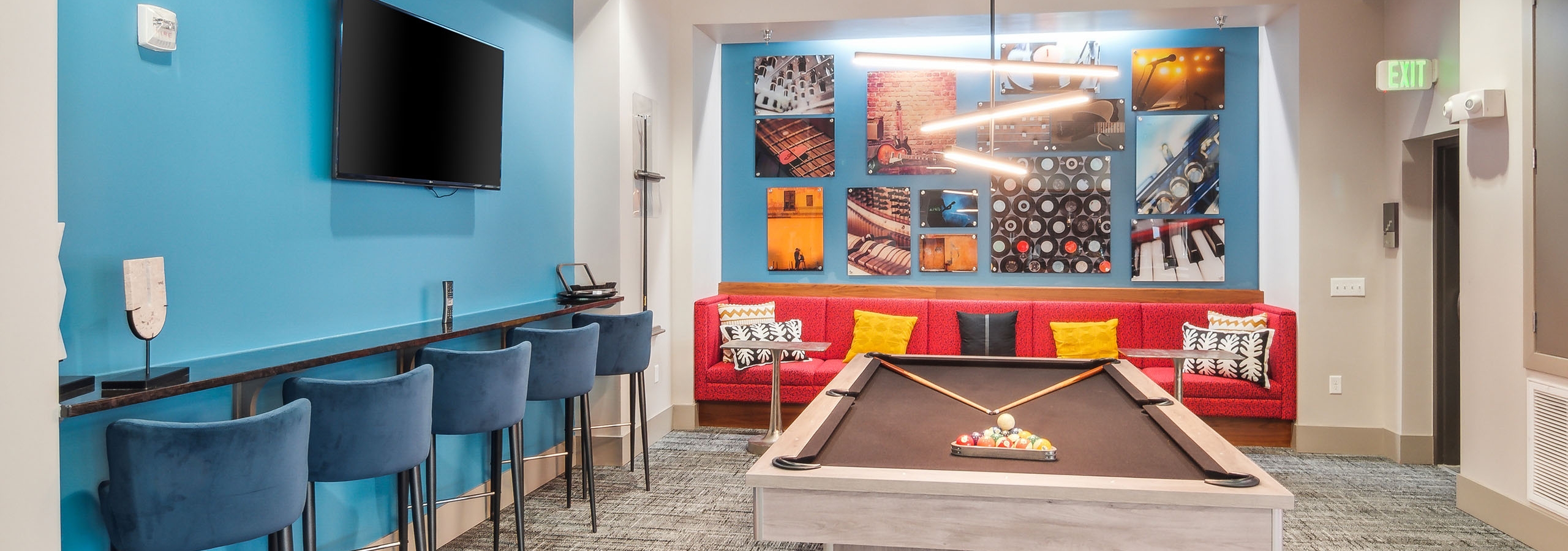 Interior view of the billiards table area at AMLI Denargo Market clubroom with red couch and blue walls with a TV and artwork