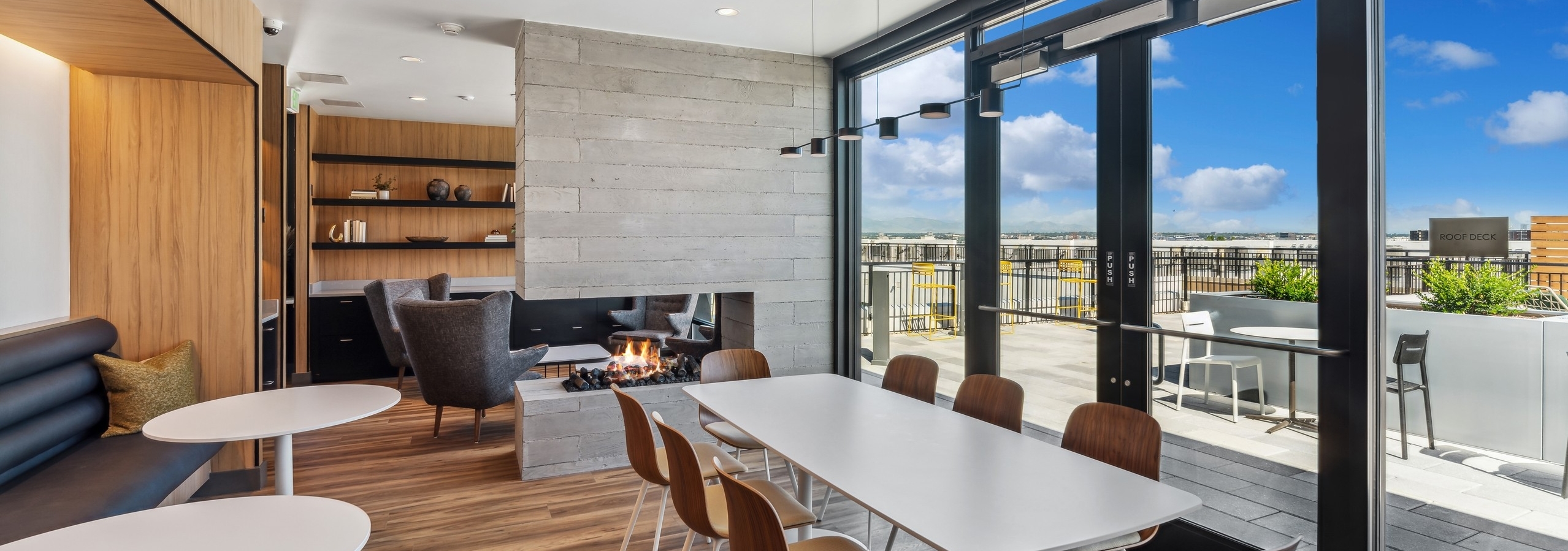 Rooftop library lounge at AMLI Broadway Park with wood floors and large table with chairs and fireplace with wall of windows
