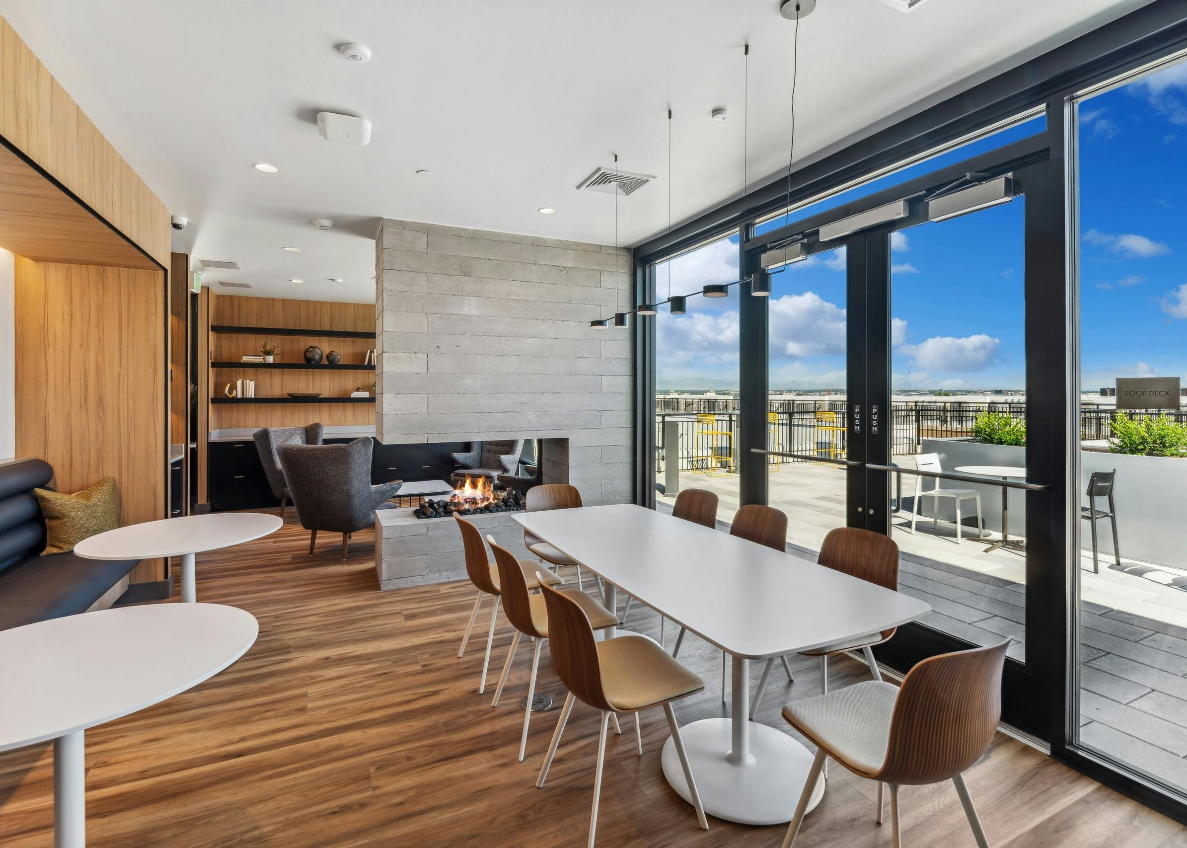 Rooftop library lounge at AMLI Broadway Park with wood floors and large table with chairs and fireplace with wall of windows