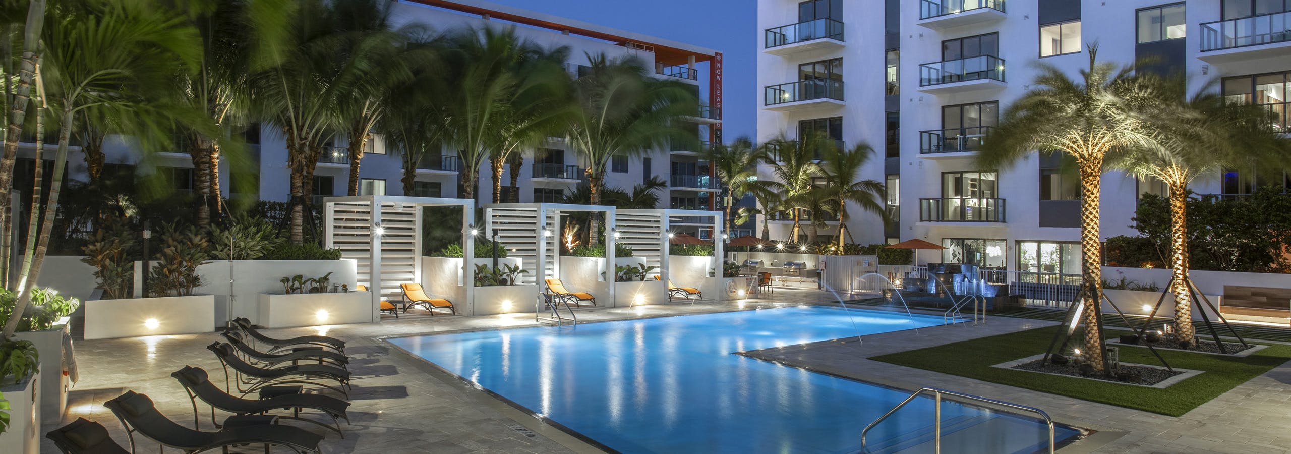 Nighttime view of the pool at AMLI Midtown Miami surrounded by lush landscape and lounge seating and three private cabanas