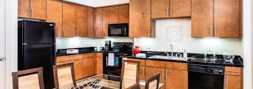 A kitchen at AMLI Park Avenue apartments with a dining table and dishwasher and sink and fridge and microwave and cabinets