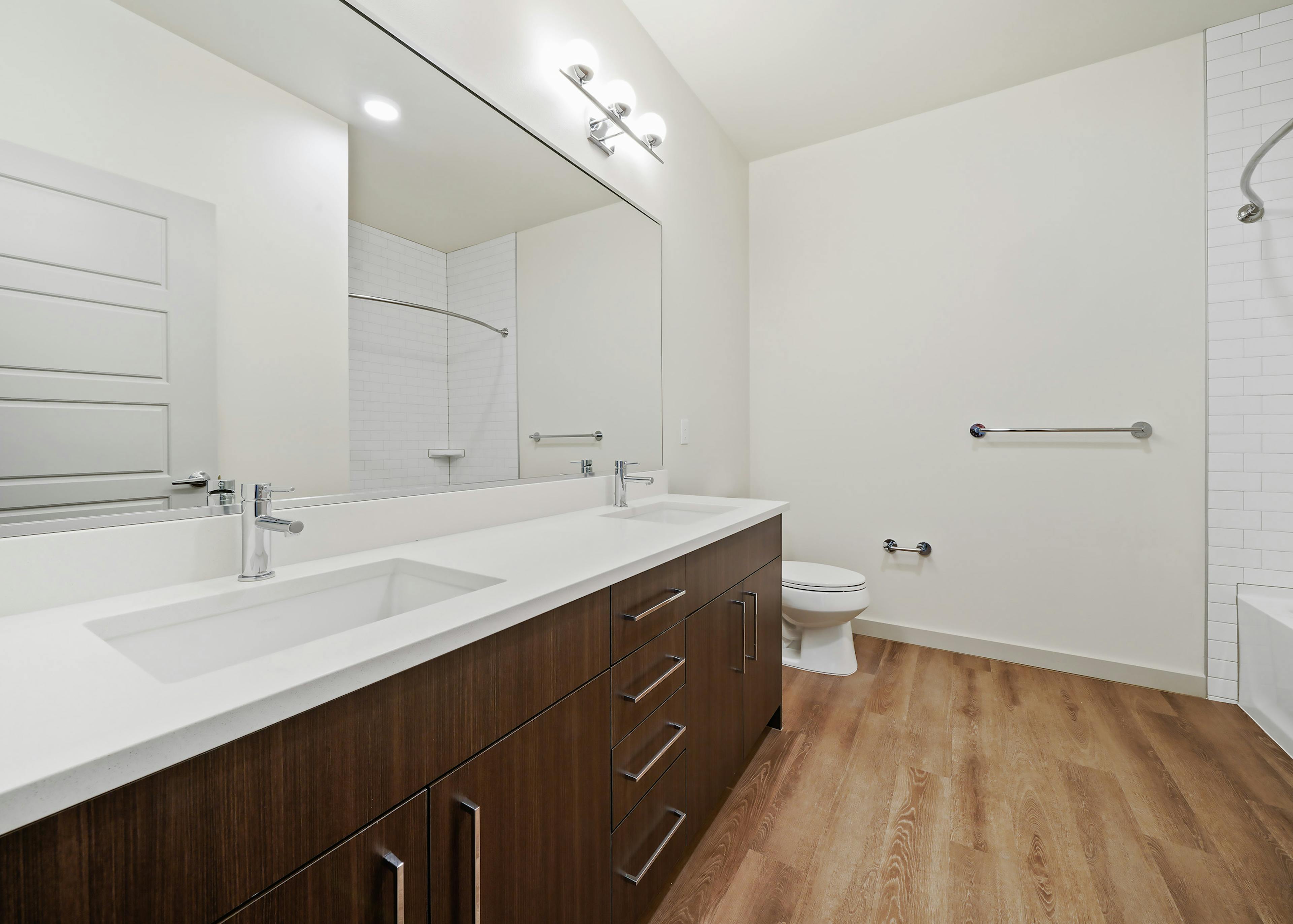 Interior view of AMLI Spring District apartment bathroom with double vanity white quartz countertop and dark brown cabinets