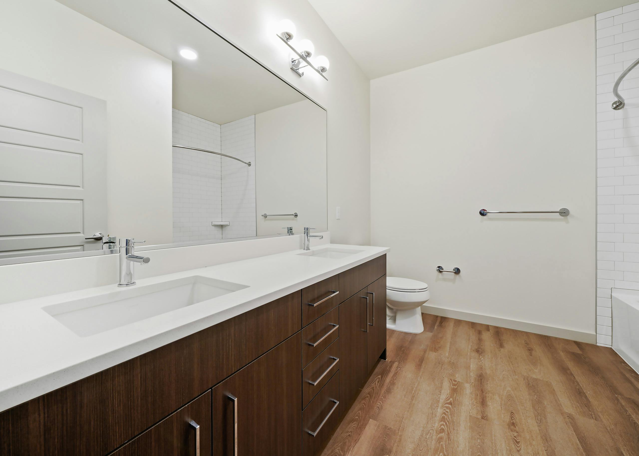 Interior view of AMLI Spring District apartment bathroom with double vanity white quartz countertop and dark brown cabinets