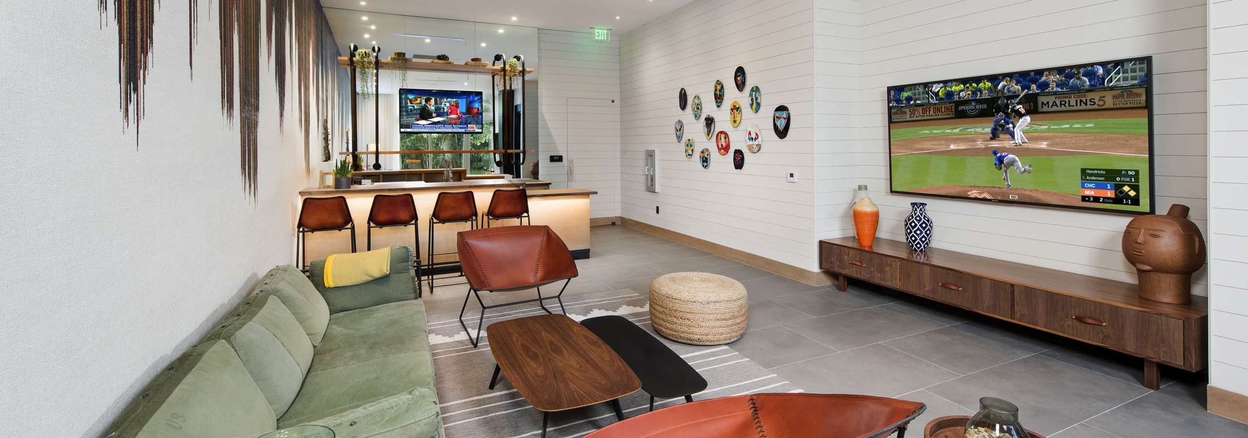 AMLI Midtown29 resident lounge with seating and large TV and drip paint accent on white walls and bar with TV in rear