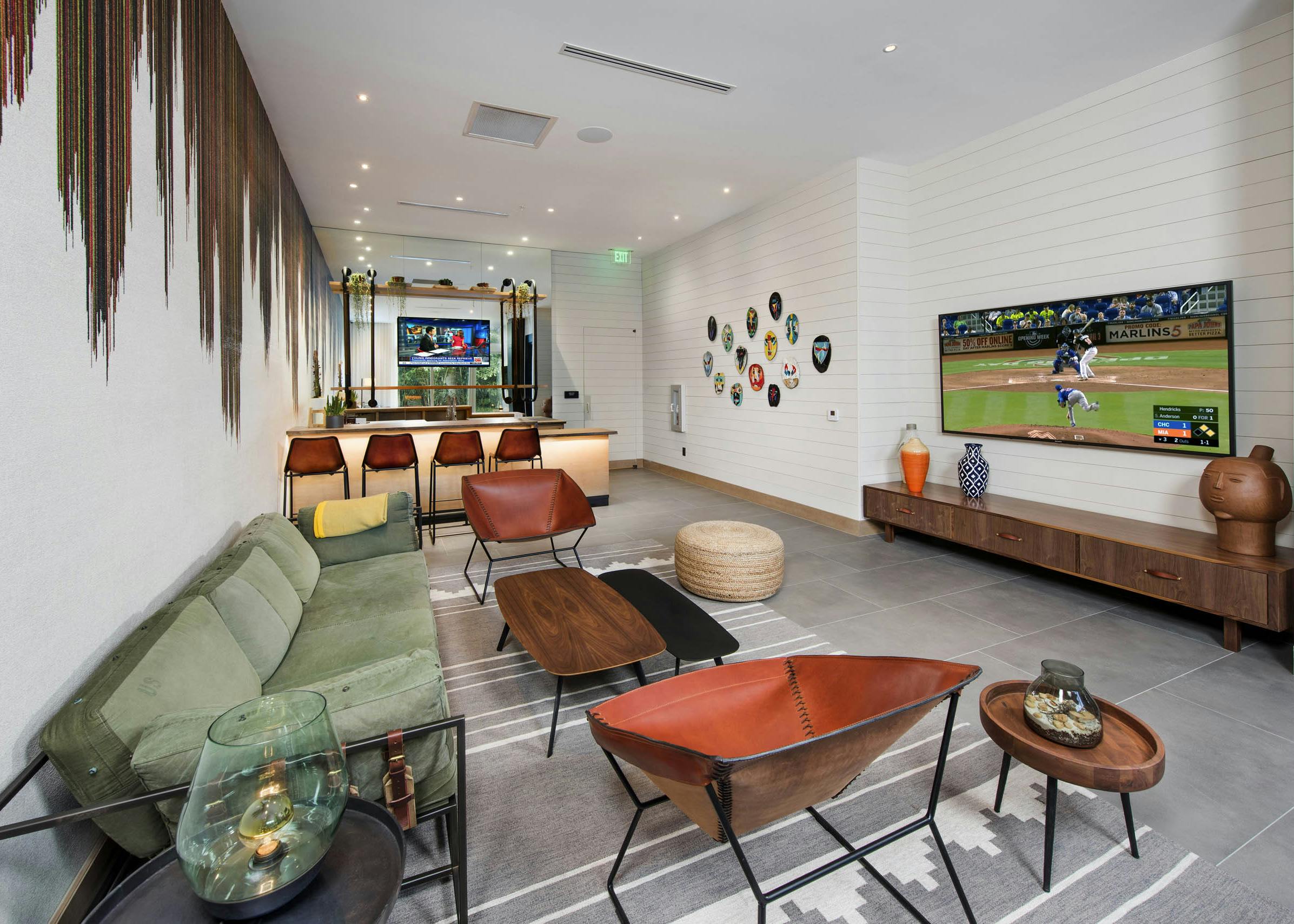 AMLI Midtown29 resident lounge with seating and large TV and drip paint accent on white walls and bar with TV in rear