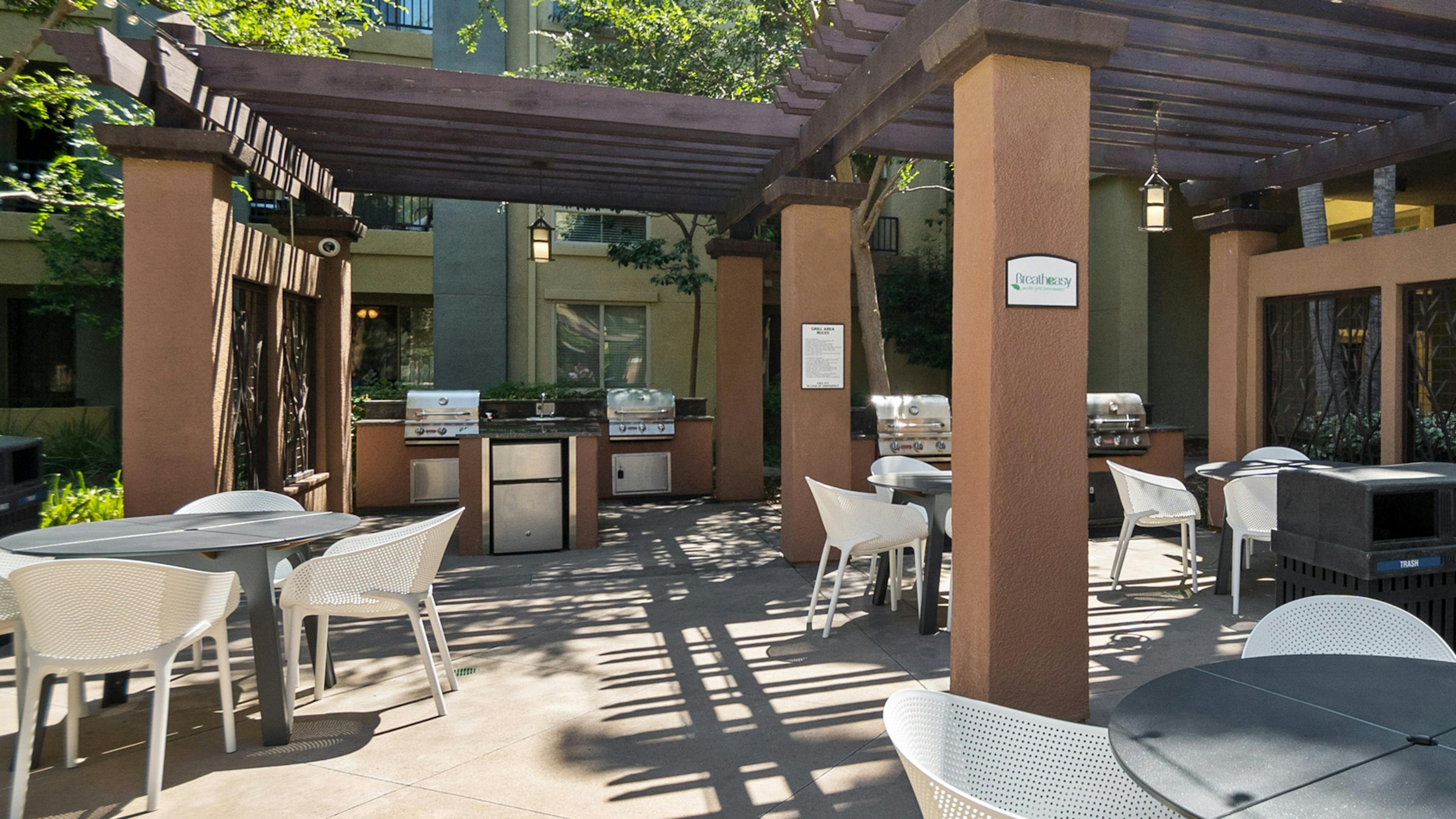 A shaded outdoor courtyard at AMLI Warner Center apartment building with grilling stations and gray tables and white chairs