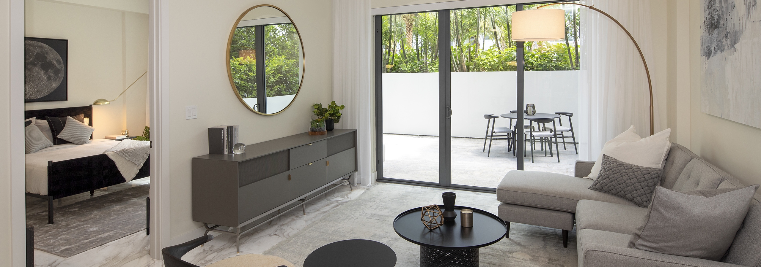Interior view of AMLI Midtown Miami living room with sofa and two chairs and view of patio and peek into the bedroom