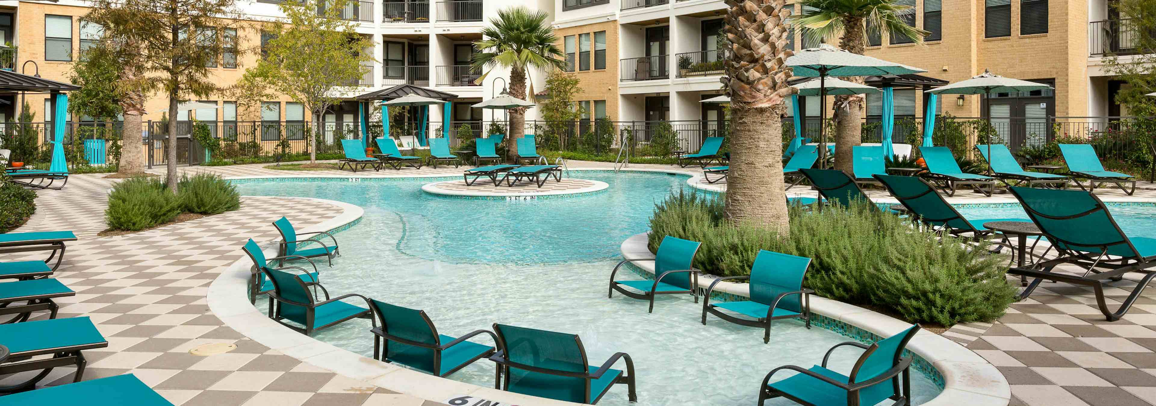 Daytime view of AMLI Campion Trail swimming pool area with lounge seating, cabanas, umbrellas and palm trees