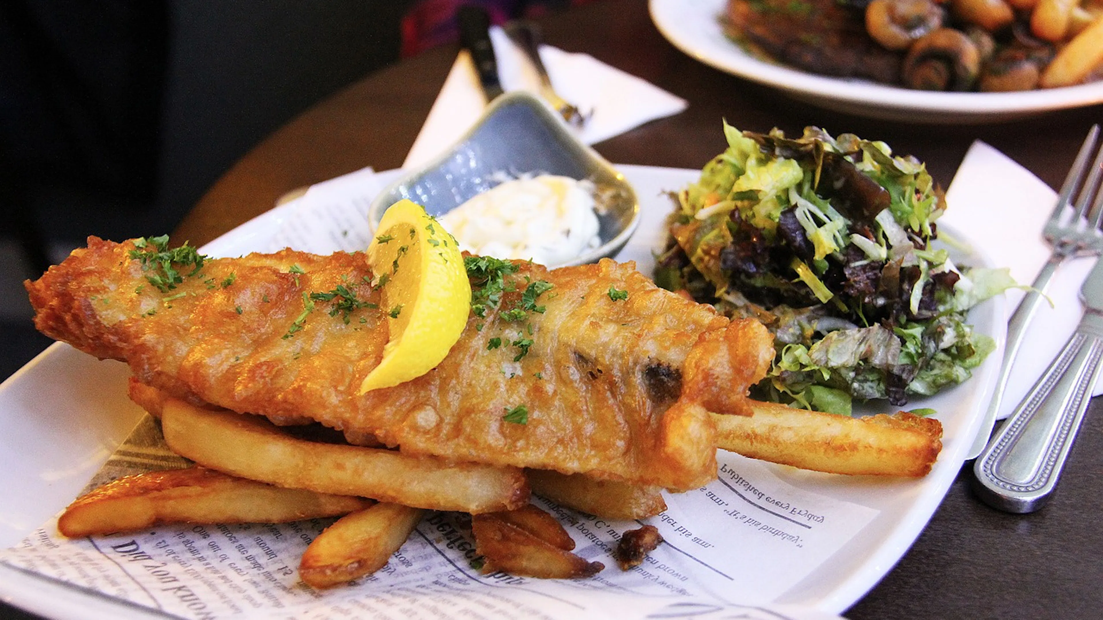 Fish and chips on a plate next to a small salad serving and a dish of tartar sauce