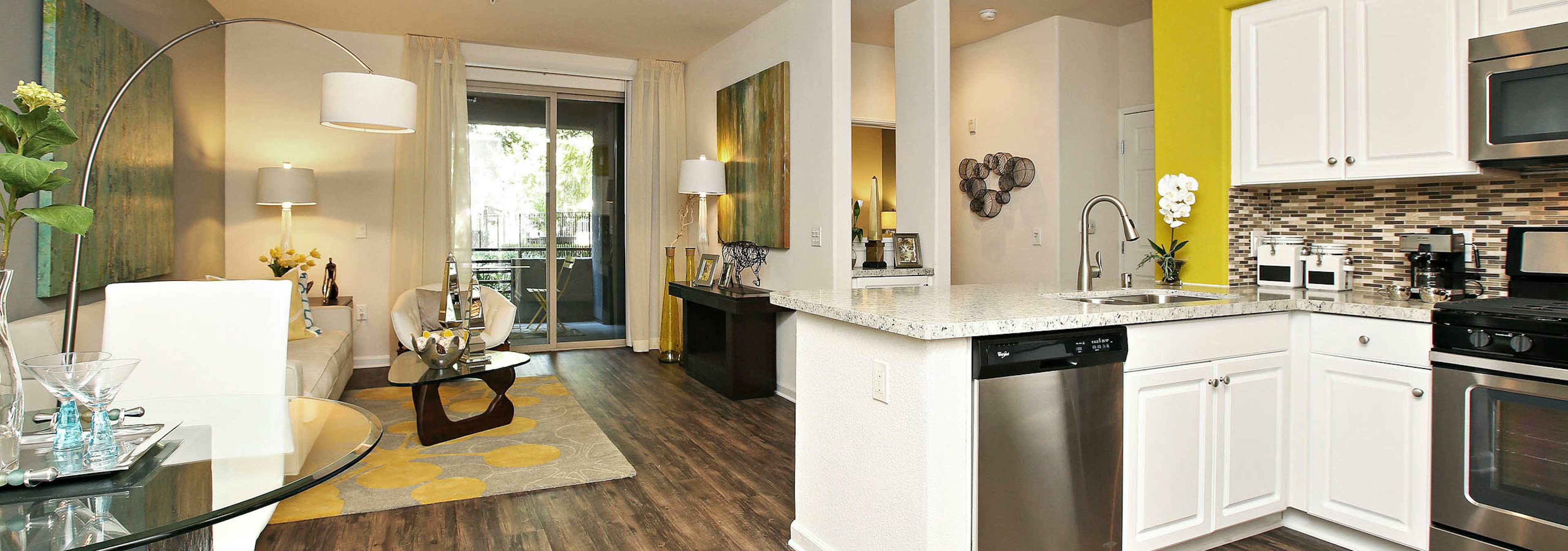 Interior of AMLI Warner Center kitchen and furnished living room with hard wood floors, white couch and centered wall art 