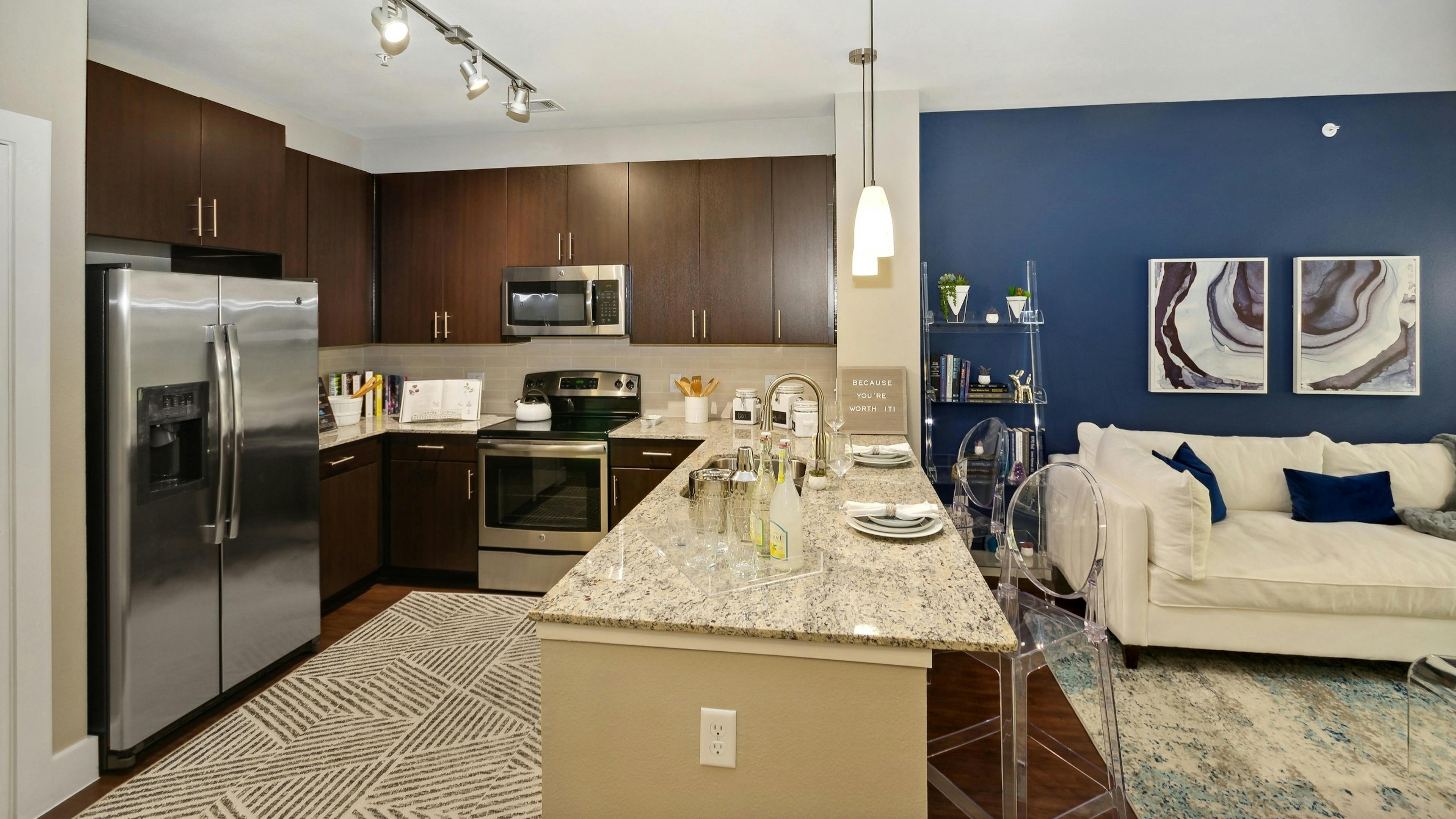 AMLI Campion Trail apartment kitchen with dark wood cabinets and stainless appliances and living room with couch on blue wall