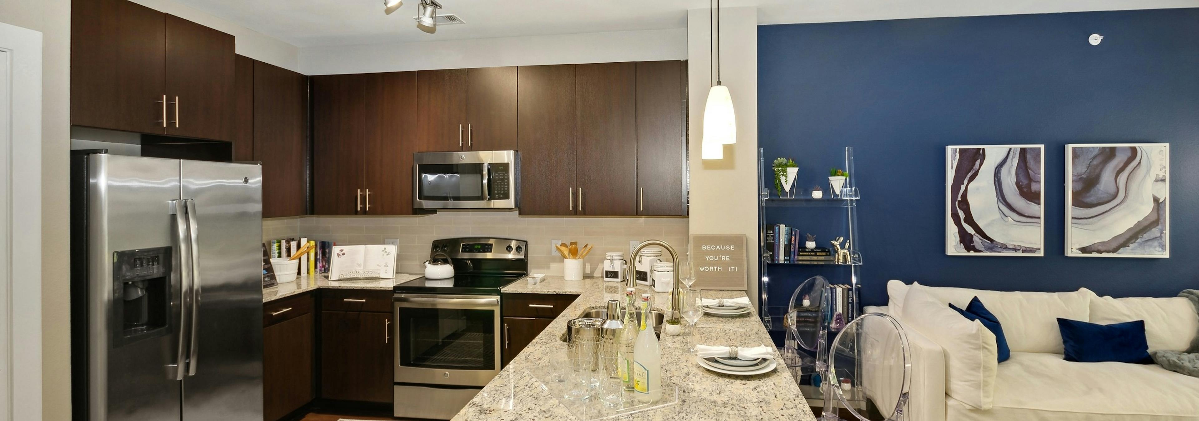 AMLI Campion Trail apartment kitchen with dark wood cabinets and stainless appliances and living room with couch on blue wall