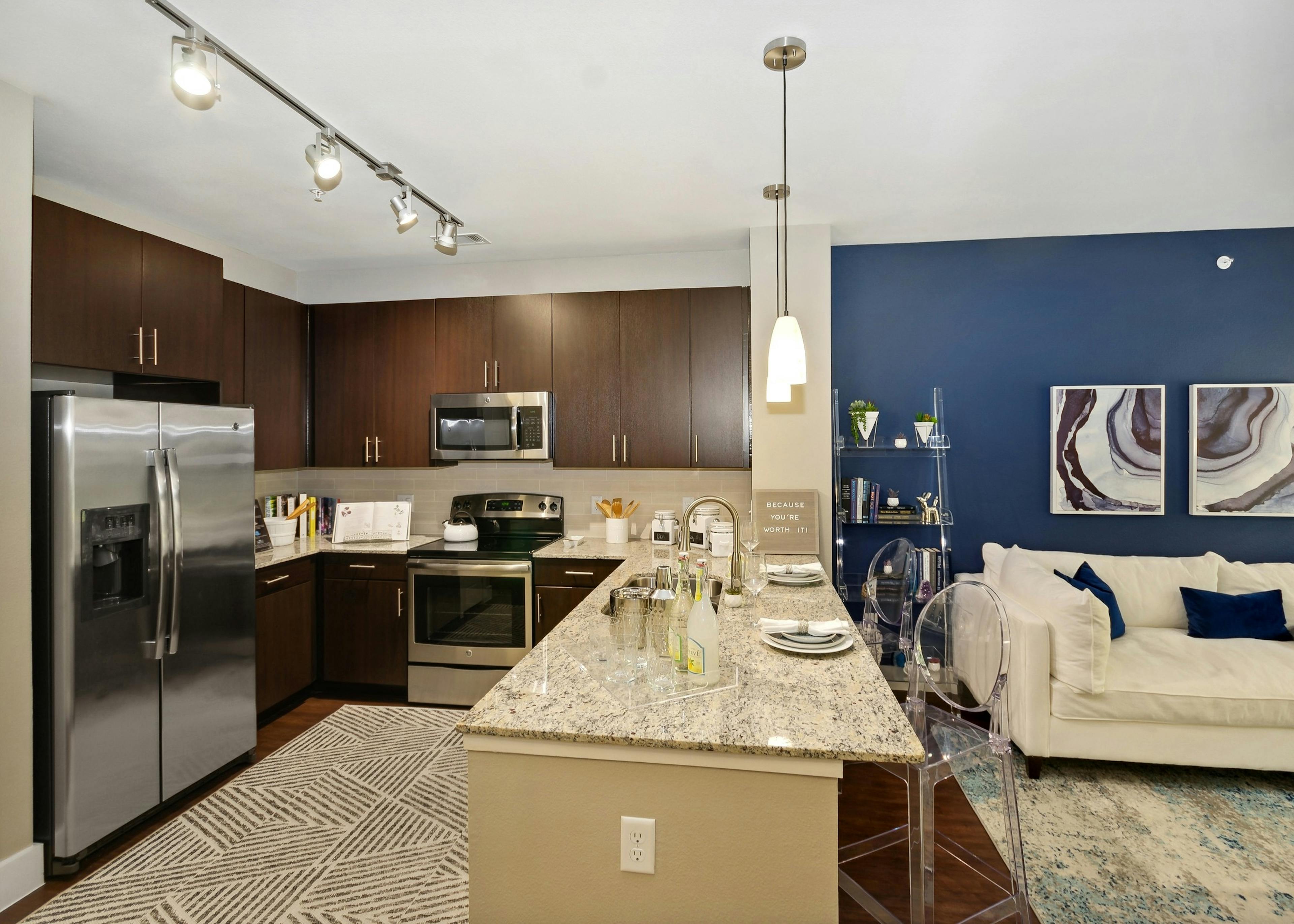 AMLI Campion Trail apartment kitchen with dark wood cabinets and stainless appliances and living room with couch on blue wall
