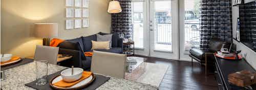 View of AMLI West Plano living room from kitchen island with dark hardwood and balcony doors with black and orange decor