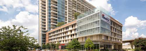 Daytime exterior view of AMLI Design District apartment building with large sign and trees at ground level with cloudy sky