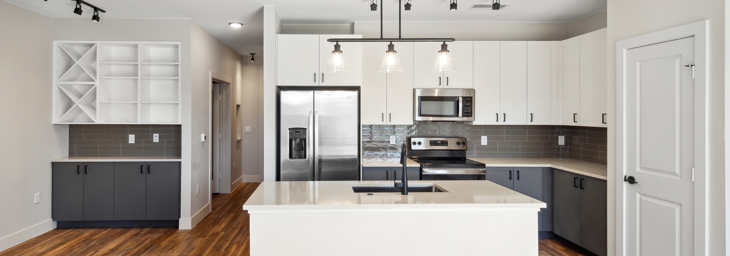 AMLI RiNo island kitchen with white upper and grey lower cabinets and black pendant and track lighting and built in shelves