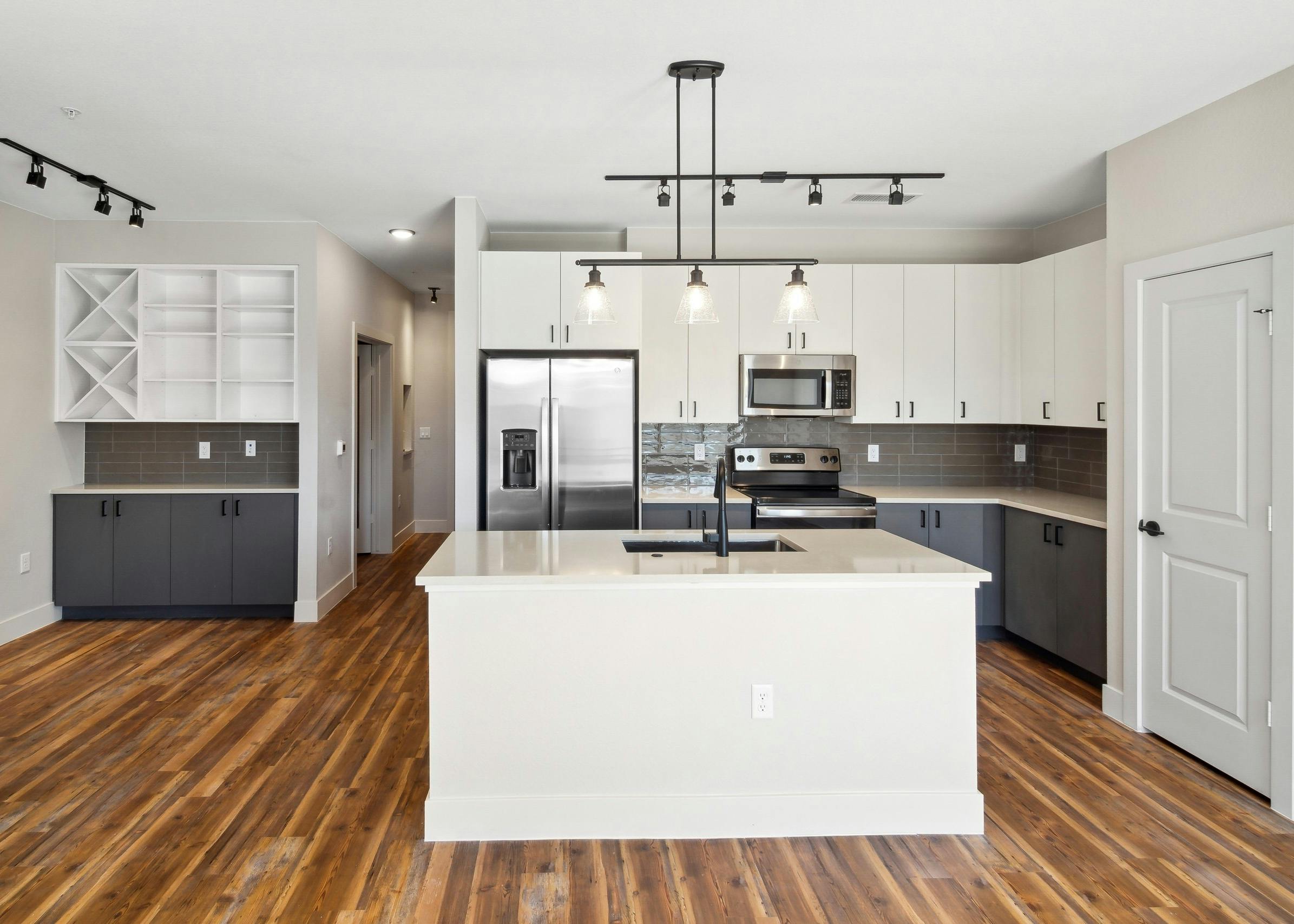AMLI RiNo island kitchen with white upper and grey lower cabinets and black pendant and track lighting and built in shelves