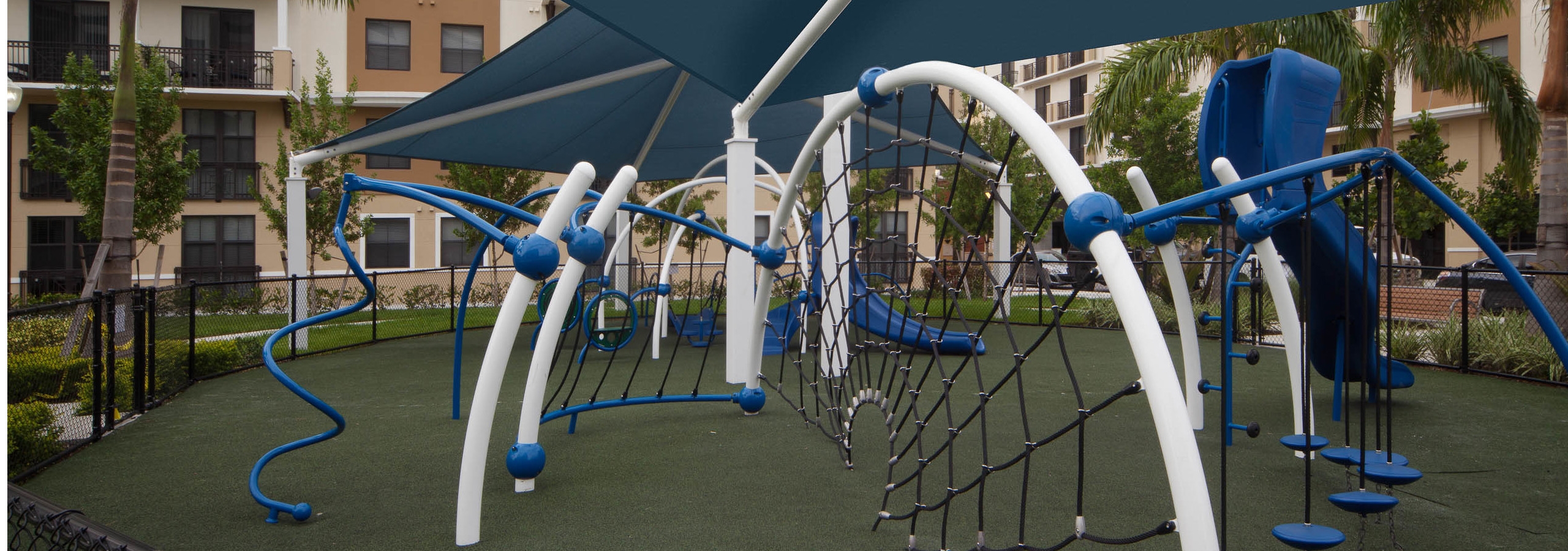 Modern Children’s covered playground at AMLI Dadeland with blue and white recreational equipment on faux grass foundation