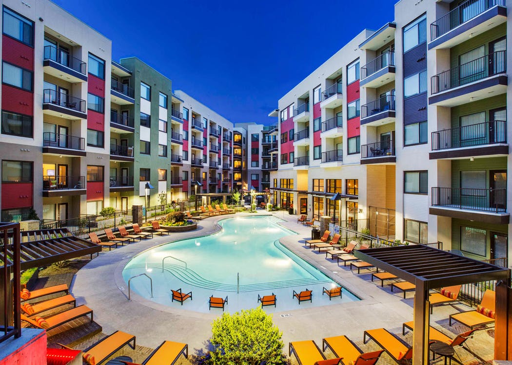 Nighttime view of the AMLI Ponce Park apartment swimming pool shaped like a teardrop and orange lounge seating with cabanas