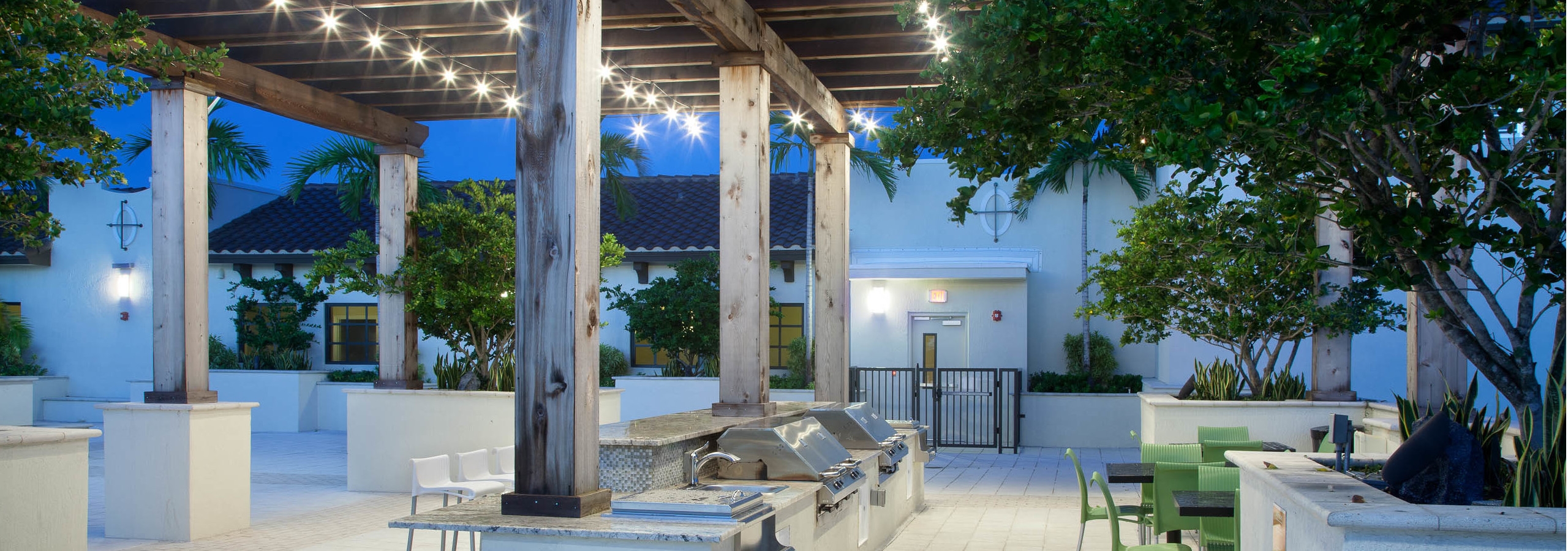 Evening view of AMLI Dadeland Rooftop gazebo with barbeque grilling area and patio furniture bordered by lush landscape